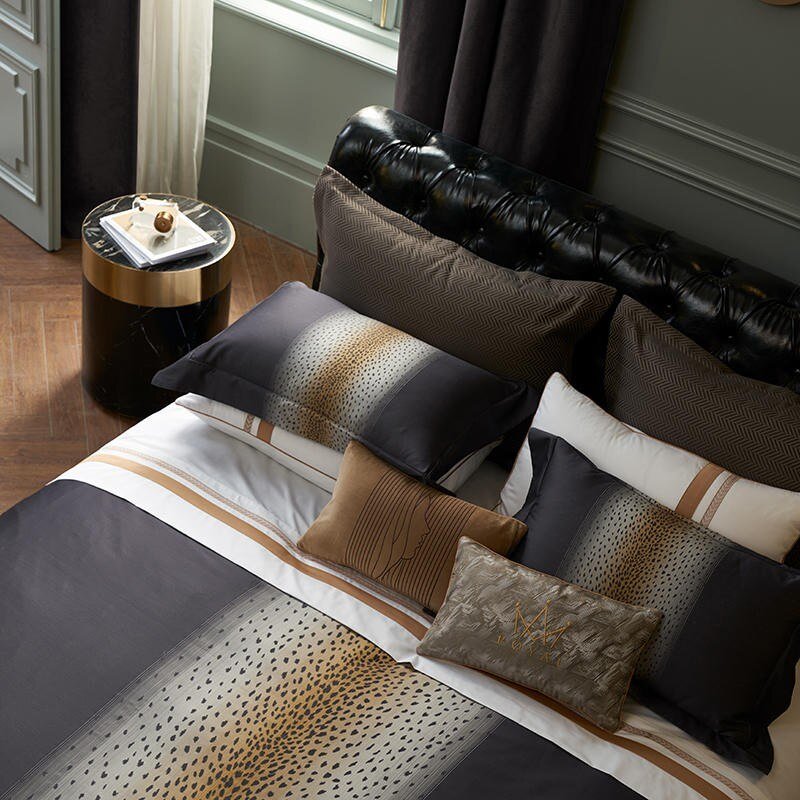 A contemporary bedding design featuring leopard print details paired with elegant brown and gold accents, complemented by a tufted black headboard and a sleek gold-accented bedside table.