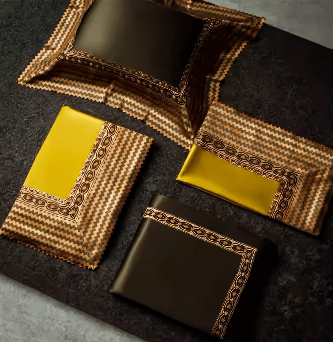 Luxury bedding set laid out, featuring pillowcases and sheets in golden yellow and deep olive green. The fabric is adorned with intricate zigzag embroidery in gold, black, and orange, with delicate circular detailing along the borders. The sheets have a smooth, satin-like texture, while the pillowcases showcase bold, contrasting designs.