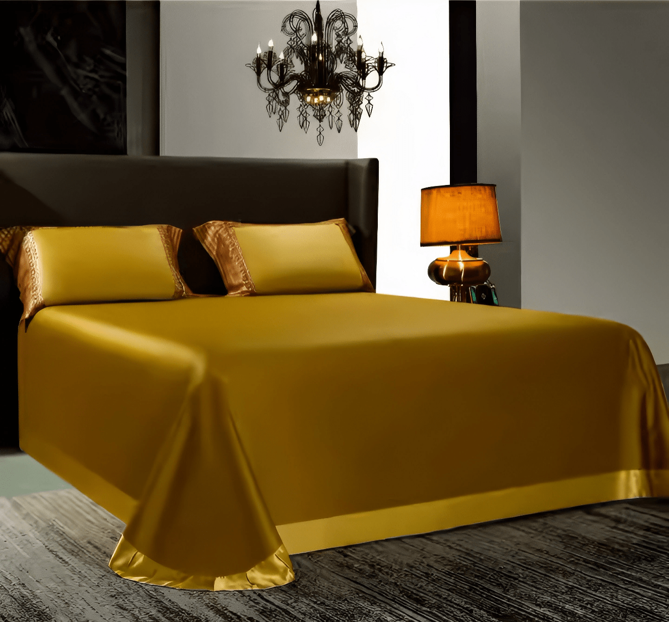 Elegant golden bedding set with a smooth satin finish, draped over a modern bed. The matching pillowcases feature delicate patterned borders. A warm amber table lamp and black chandelier add sophistication to the contemporary bedroom setting.