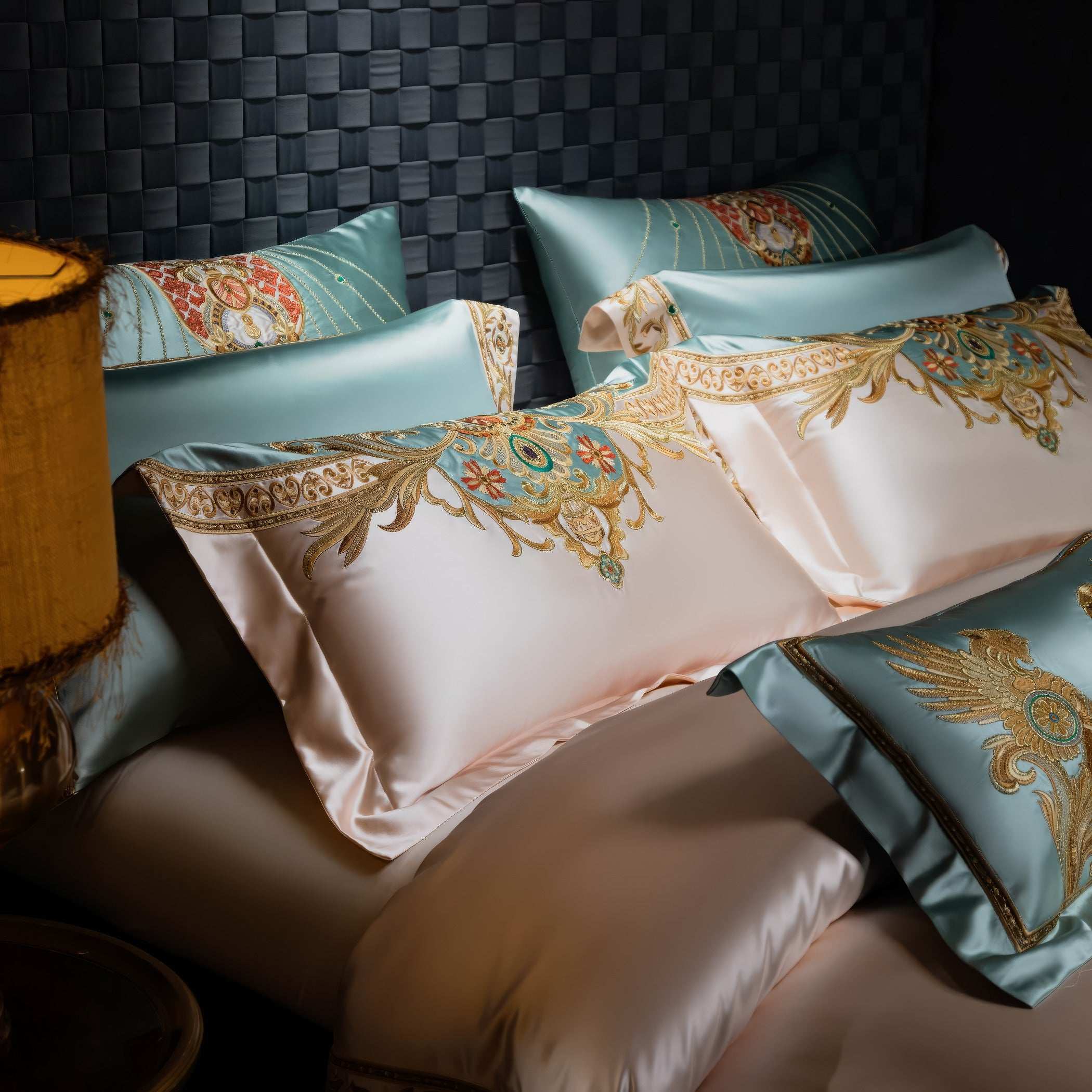 Close-up of luxurious pillowcases in light blue and cream with intricate gold and turquoise embroidery, showcasing baroque-inspired patterns and smooth satin texture, styled on a sophisticated bedding set.