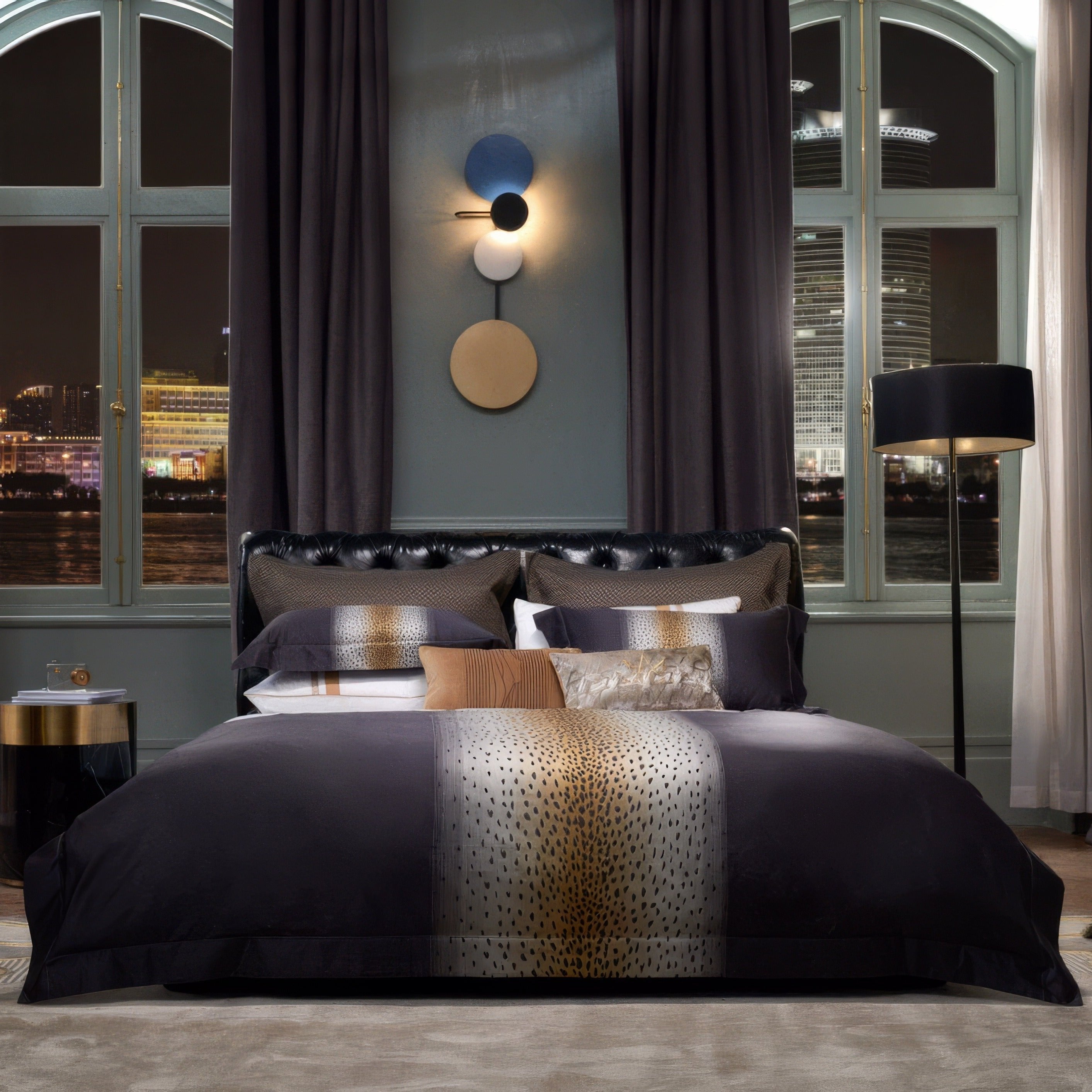 Modern bedding set featuring a black and metallic gold Egyptian cotton duvet cover with a central leopard print-inspired design. Accented with coordinating pillowcases and decorative cushions in textured patterns. Set in a contemporary bedroom with arched windows offering a nighttime city view, complemented by neutral-toned furnishings and statement lighting.