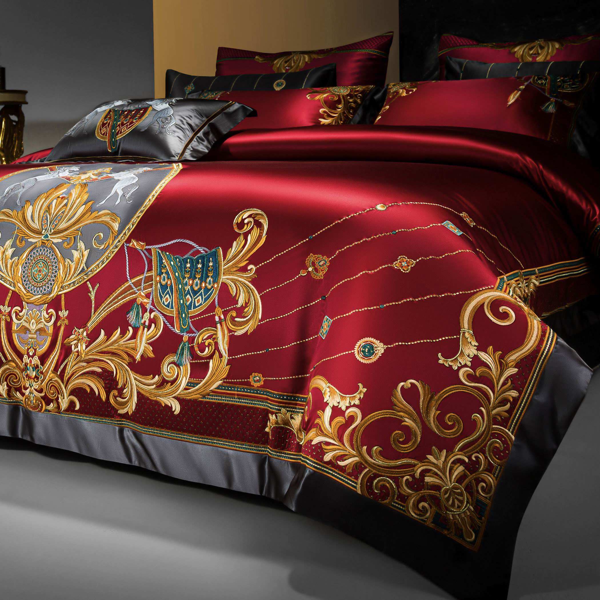 A close-up view of a luxurious bedding set in a deep red satin adorned with intricate golden embroidery. The elaborate patterns include regal scrollwork, delicate chain-like designs, and ornate accents with teal and emerald green highlights. The black border framing the edges adds depth and sophistication, complementing the vibrant red and gold palette. The craftsmanship and attention to detail convey a sense of opulence, making this bedding set a centerpiece for an elegant bedroom.