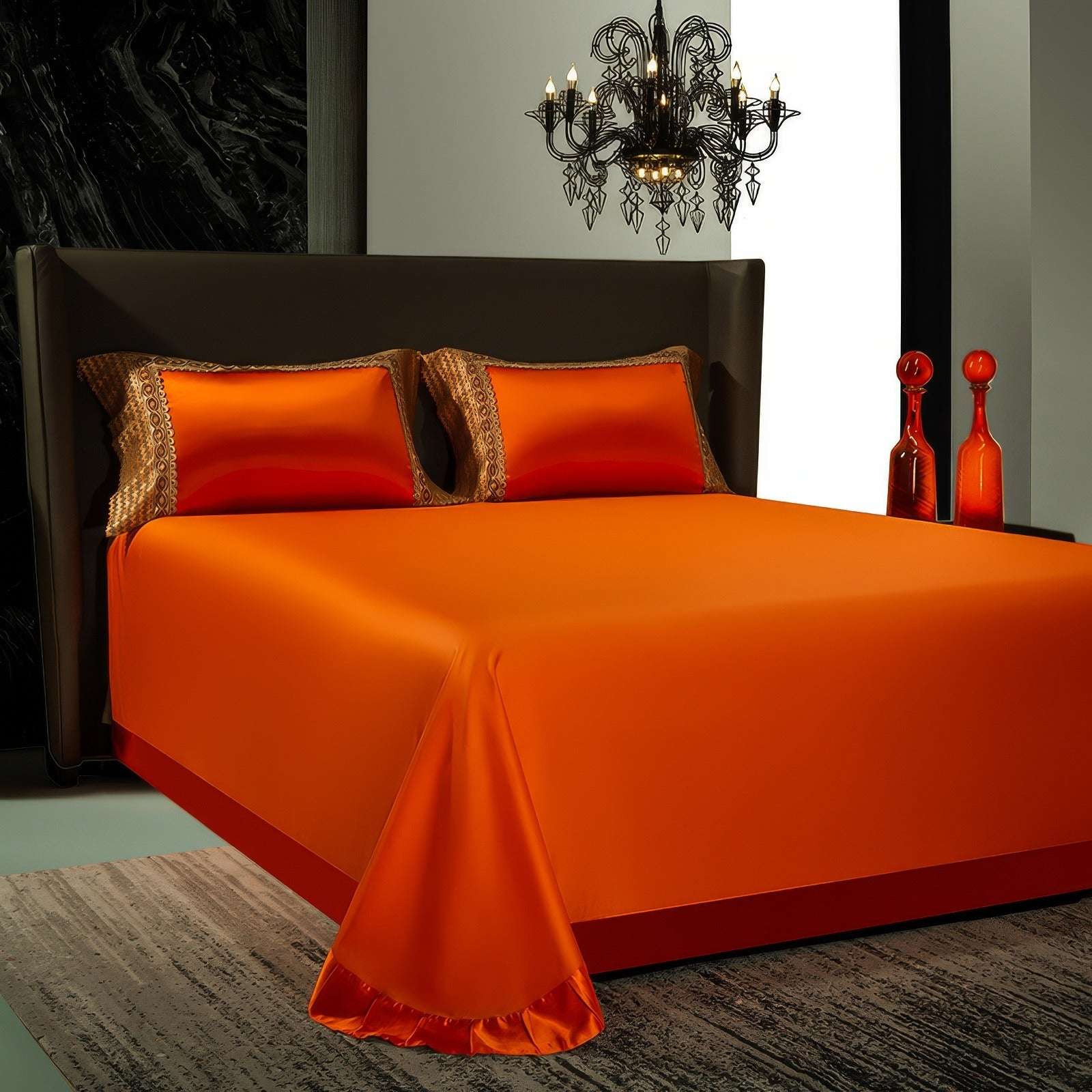 A bedroom featuring vibrant orange satin bedding with two matching pillowcases adorned with intricate gold and brown decorative borders. The sleek black bed frame contrasts against the bright bedding, while a luxurious chandelier and red glass vases add a dramatic touch to the modern decor.