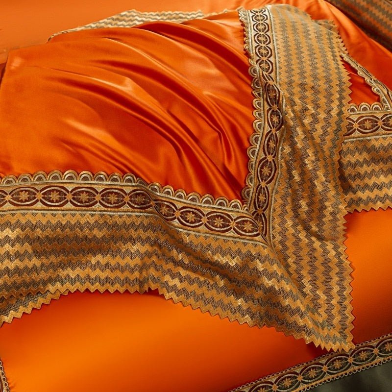 Bright orange satin bedding with an intricate decorative border featuring a chevron pattern in shades of gold, brown, and black. The fabric appears smooth and glossy, draped with folds, emphasizing its luxurious texture.