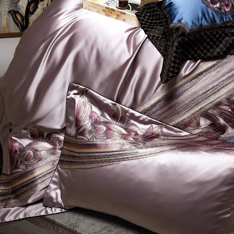 Close-up of lavender silk bedding featuring detailed floral embroidery in pink and purple hues, with flowing patterns extending across the fabric. A matching pillowcase showcases the same intricate design, adding elegance and texture to the luxurious ensemble.