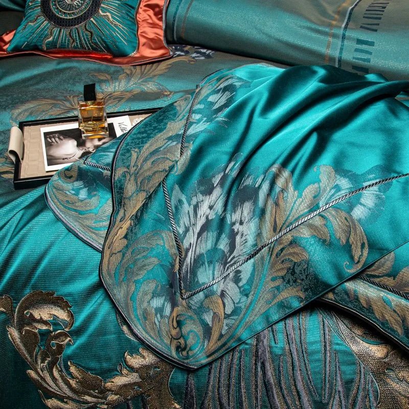 A close-up view of a teal bedding set showcasing intricate gold and silver floral embroidery on a luxurious satin fabric. The foreground highlights an elaborately patterned corner with baroque-inspired detailing and precise stitching. A black tray sits on the bed, holding a gold perfume bottle and a magazine, enhancing the luxurious aesthetic. The coral-accented decorative pillow in the background adds a touch of contrast and sophistication.