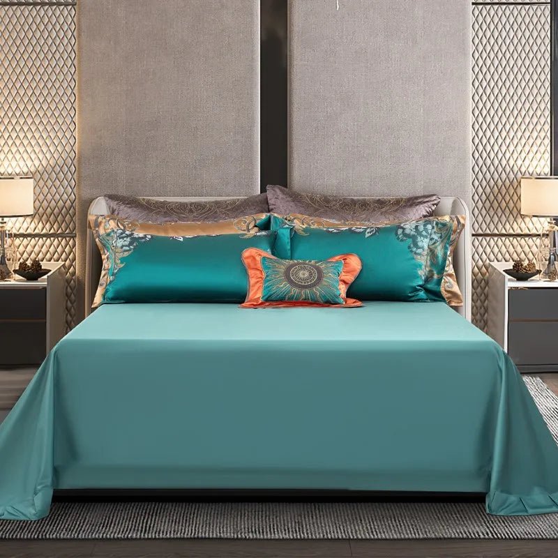 A neatly styled bedding set featuring a teal bedspread paired with matching teal pillowcases that have delicate floral embroidery on the edges. A vibrant coral accent pillow with a sunburst motif adds a bold centerpiece to the arrangement. In the background, champagne and grey pillows with intricate patterns provide a touch of contrast, while warm lighting from bedside lamps enhances the elegant ambiance of the room.