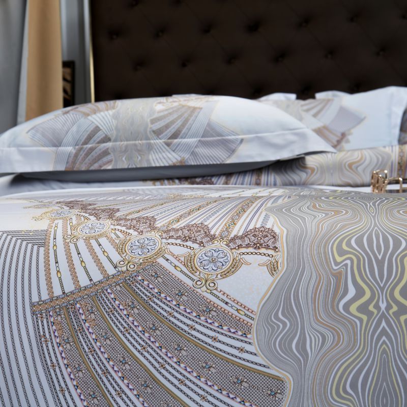 Close-up view of an elegant white duvet cover with intricate beige and gray fan-inspired patterns accented with delicate gold detailing, paired with matching pillowcases for a sophisticated and luxurious bedroom look.