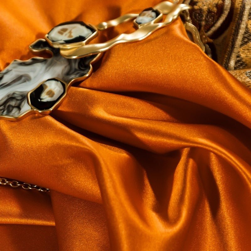 Smooth, vibrant orange silk fabric with a gold and marbled black accessory draped over it, highlighting the luxurious sheen and elegant texture.