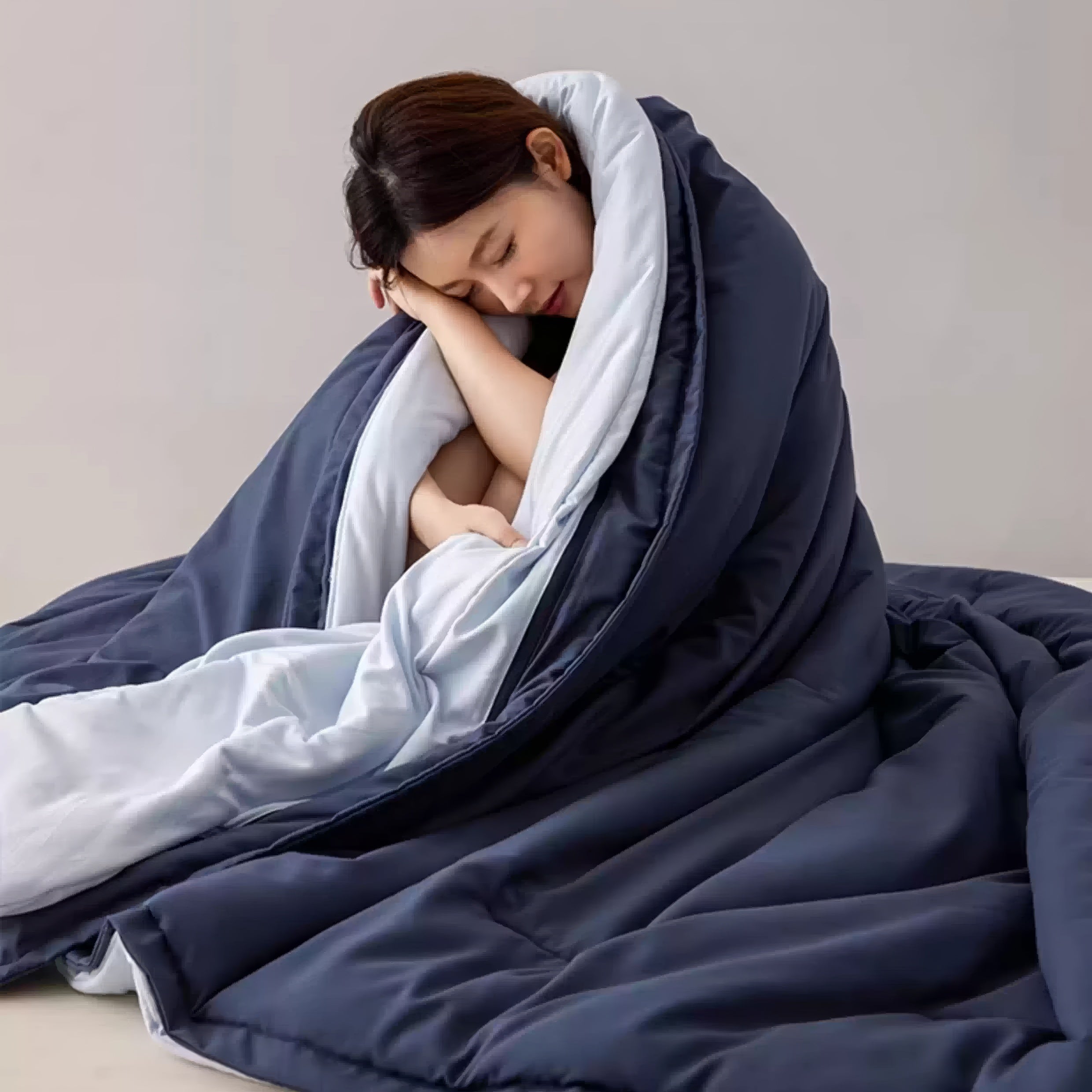 Woman wrapped in a large blue and white comforter against a plain background