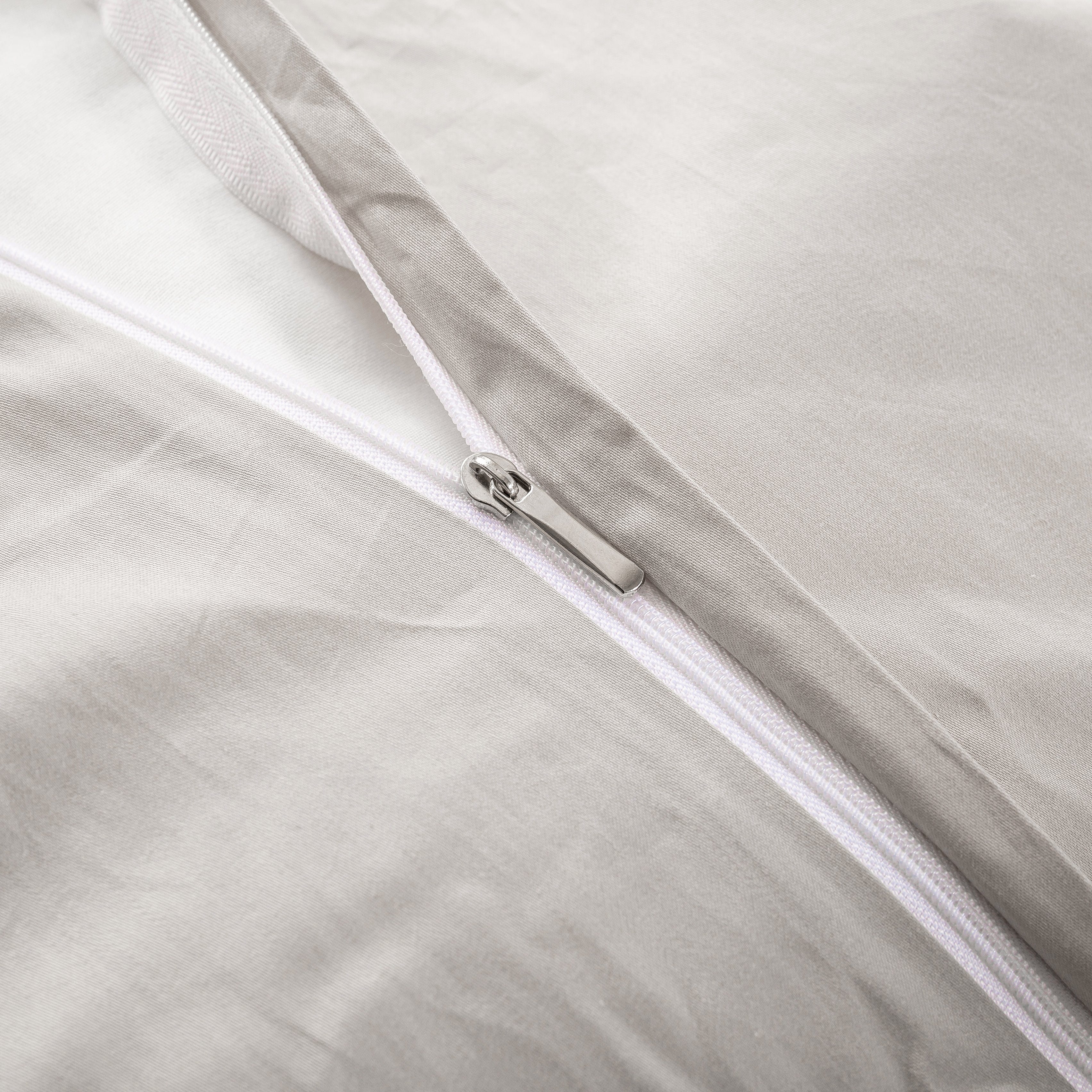 Close-up of a concealed zipper with a metallic pull tab on a light gray fabric, highlighting a smooth and seamless bedding closure design.