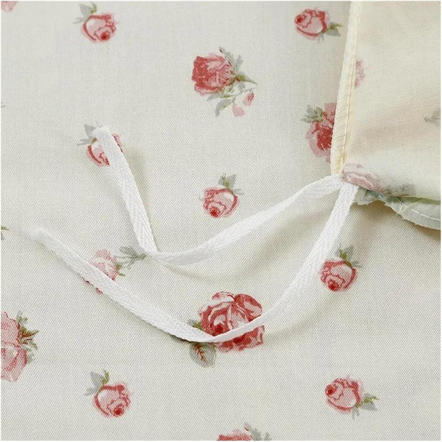 Cream-colored fabric with a dainty pink rose pattern, featuring two white tie strings sewn securely into the material, likely for securing bedding.