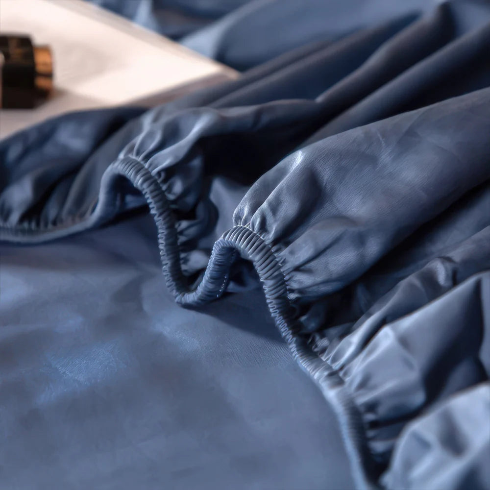 Close-up of a blue satin fitted sheet with elastic edges, showing smooth, wrinkle-free fabric and stitching details.

