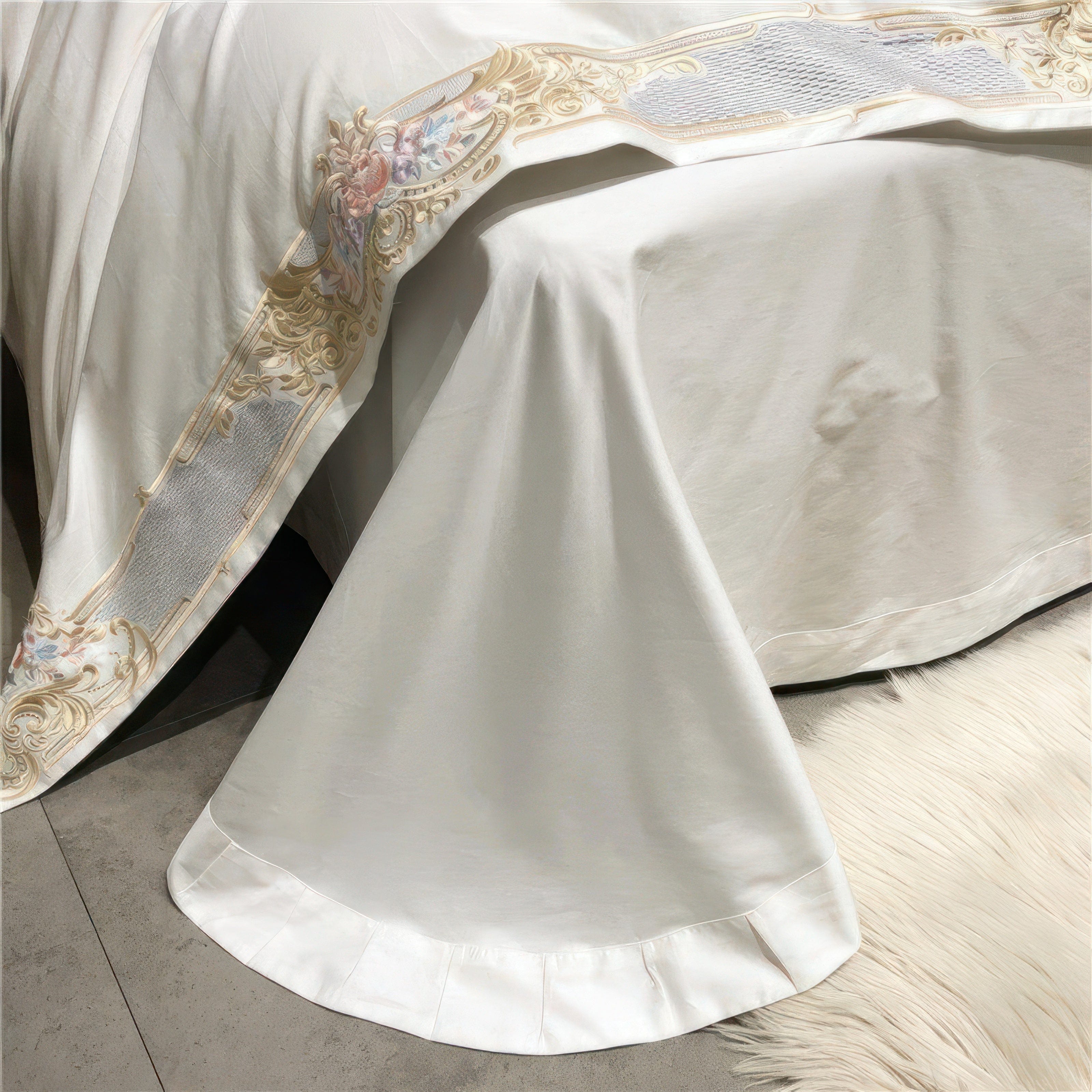 A close-up view of the corner of a white bedspread showcasing its smooth and flowing fabric, enhanced with detailed gold and pastel floral embroidery along the edge. The clean, luxurious design drapes elegantly over the bed, resting on a soft white fur rug, adding a refined and cozy touch to the setting.

