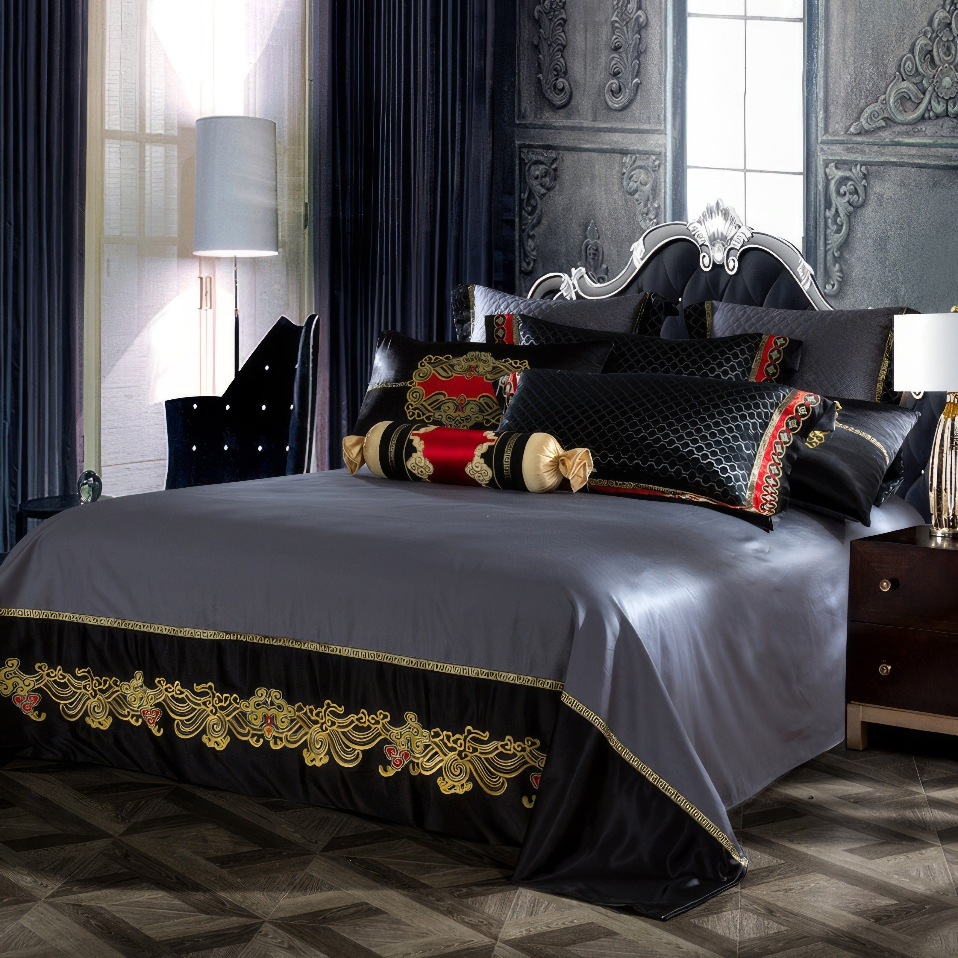 A luxurious bedding set in deep gray and black hues adorned with intricate gold embroidery and accents of vibrant red. The bed features decorative pillows, including bolsters with golden ends and elaborate patterns, against a tufted black headboard with a silver ornate frame. The room is styled with dramatic dark curtains, a sleek velvet chair, and a white floor lamp, creating a regal ambiance. The flooring displays a parquet design, enhancing the sophistication of the space.

