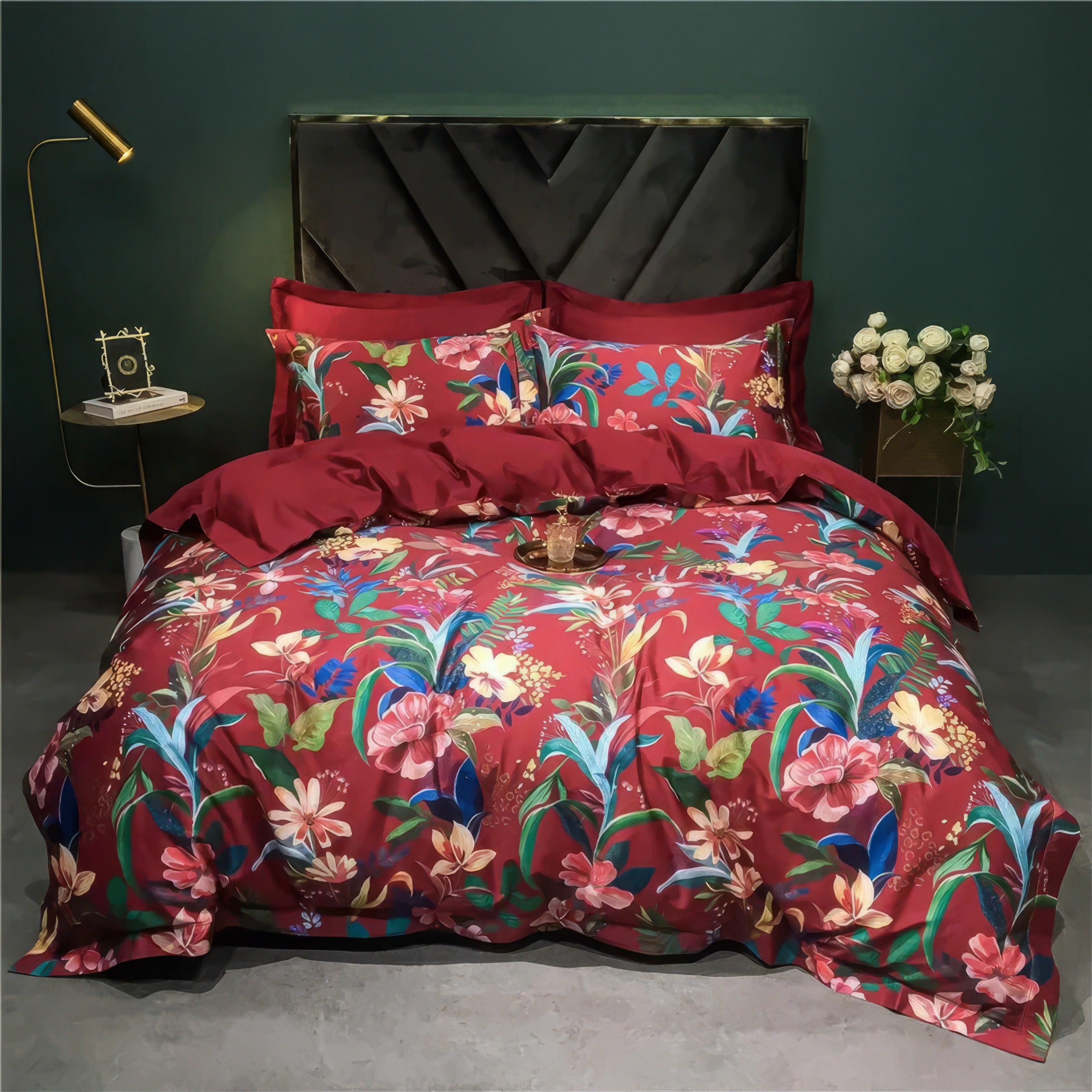 Elegant red Egyptian cotton bedding set featuring vibrant tropical floral patterns, including pink, blue, and yellow blooms with lush green leaves. The set is styled with bold crimson pillowcases and a matching duvet cover, enhancing the luxurious feel of the smooth, silky fabric. The room decor includes a gold-accented lamp, a bouquet of white roses, and a modern black headboard, adding a sophisticated touch.

