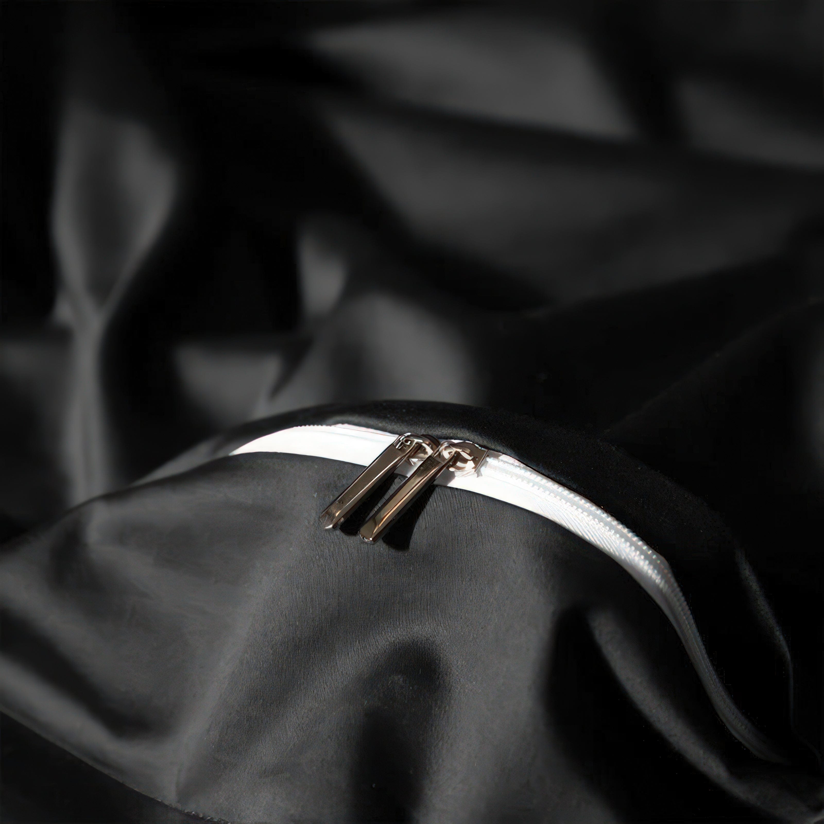 A close-up of a sleek black fabric featuring a durable white zipper with dual metallic pulls, showcasing the elegant functionality of the material.

