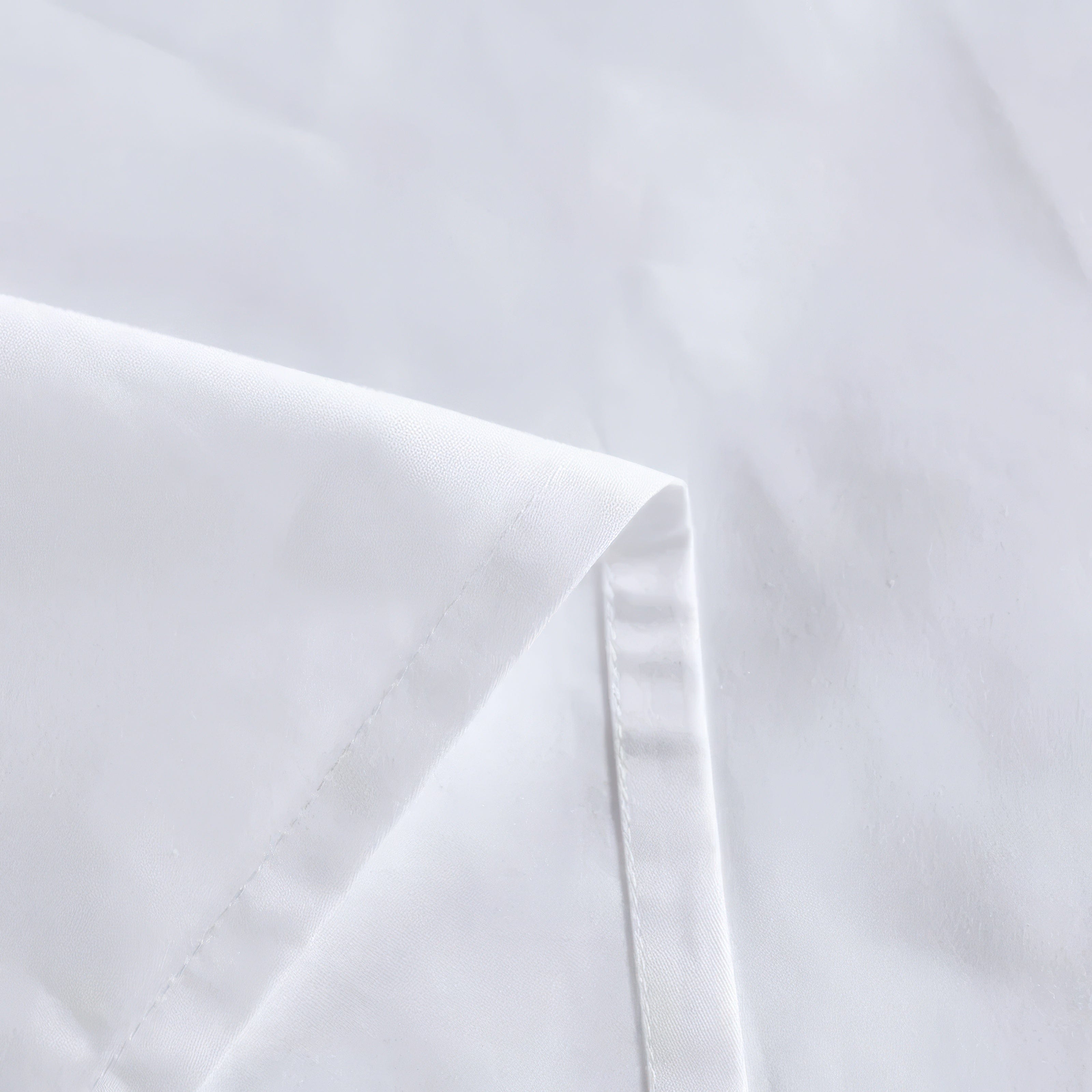 A close-up view of a crisp white fabric, highlighting the precise stitching along the edge, emphasizing its smooth texture and high-quality craftsmanship.

