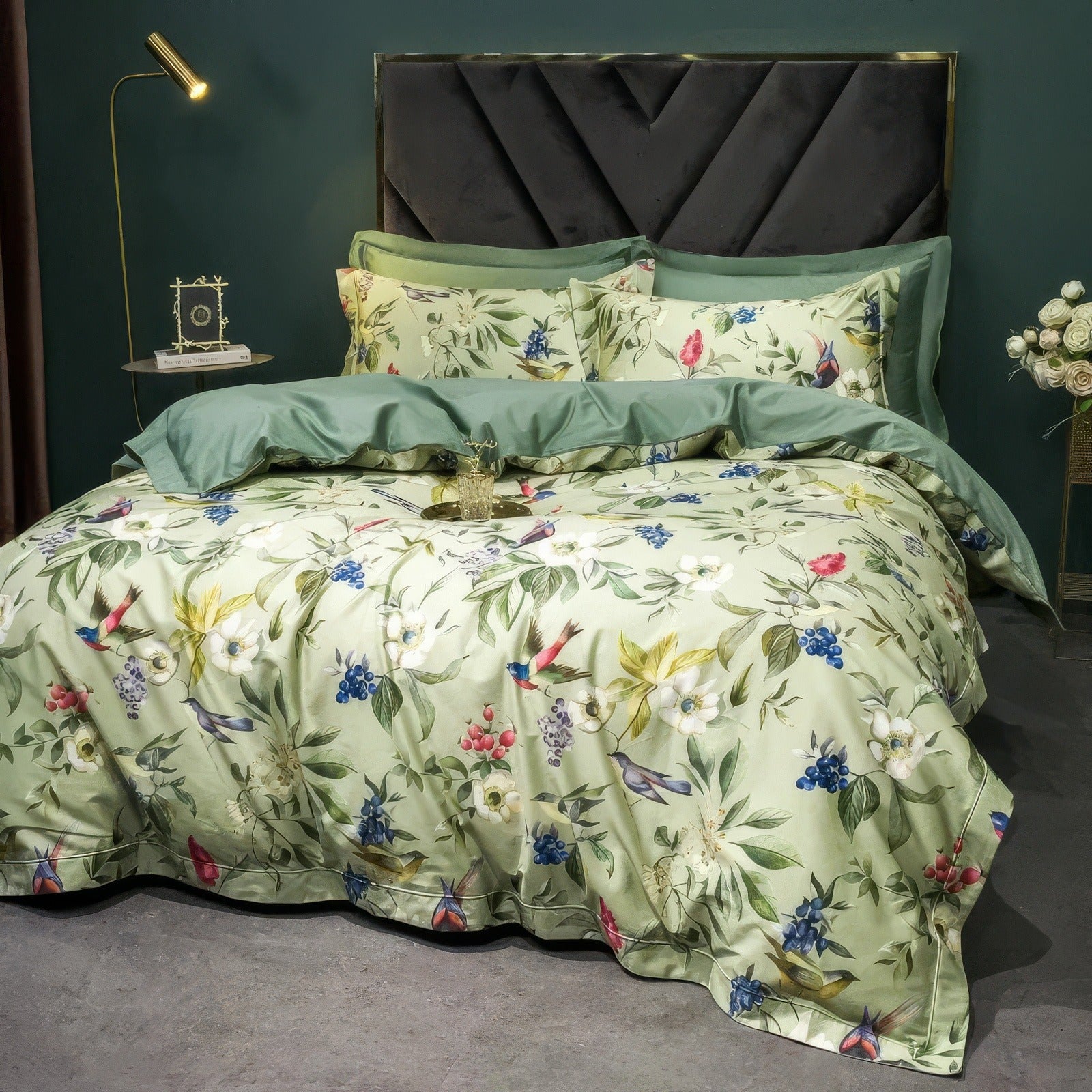 A luxurious bedding set with a botanical print featuring colorful flowers, green leaves, and vibrant birds on a light green background, complemented by matching solid green pillowcases and a duvet cover, styled in a chic bedroom with a modern green accent wall and a black upholstered headboard.

