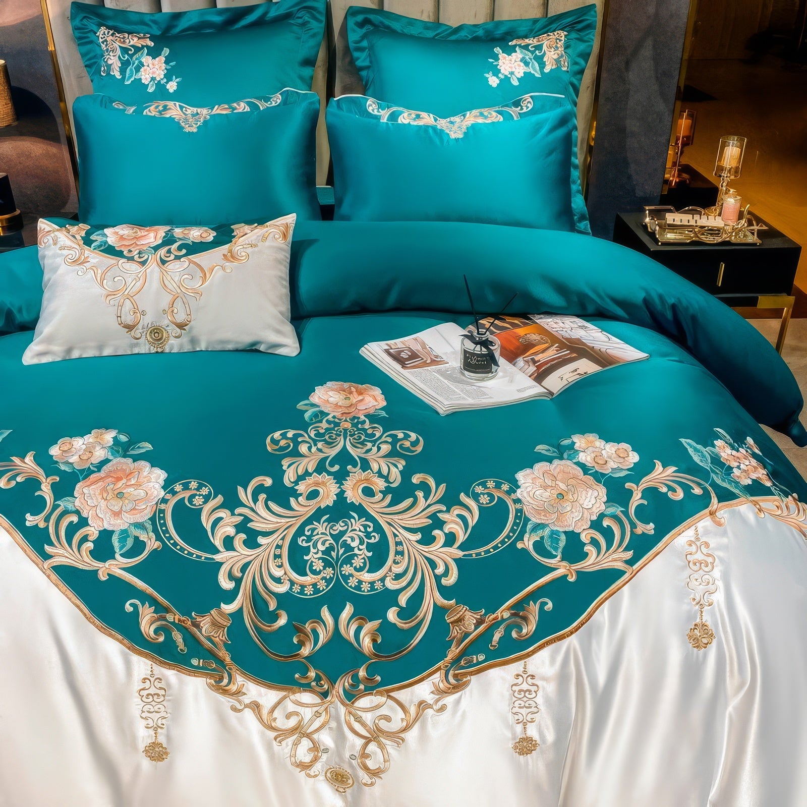 Close-up of a luxurious teal bedding set adorned with golden floral embroidery and intricate ornamental designs. The centerpiece of the duvet features detailed pink and peach blossoms with elegant green foliage, seamlessly integrated into the ornate golden patterns. A white pillow with matching embroidery adds a refined contrast, while a reed diffuser and open book provide a touch of modern sophistication to the setup.

