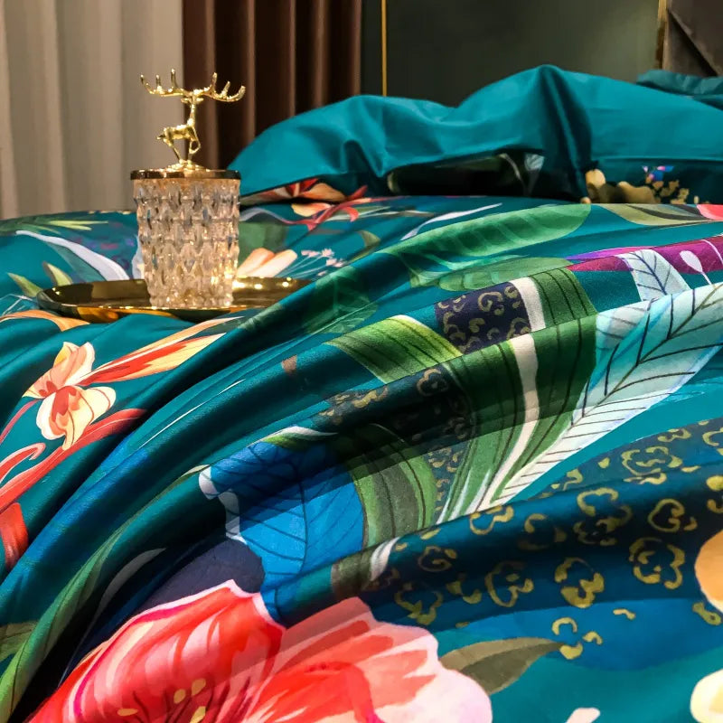 Close-up of the tropical floral bedding in rich teal Egyptian cotton, showcasing vibrant green foliage, vivid red flowers, and intricate botanical designs. The luxurious texture highlights the silky sheen, complemented by a decorative gold-accented glass and tray, adding elegance to the overall aesthetic.

