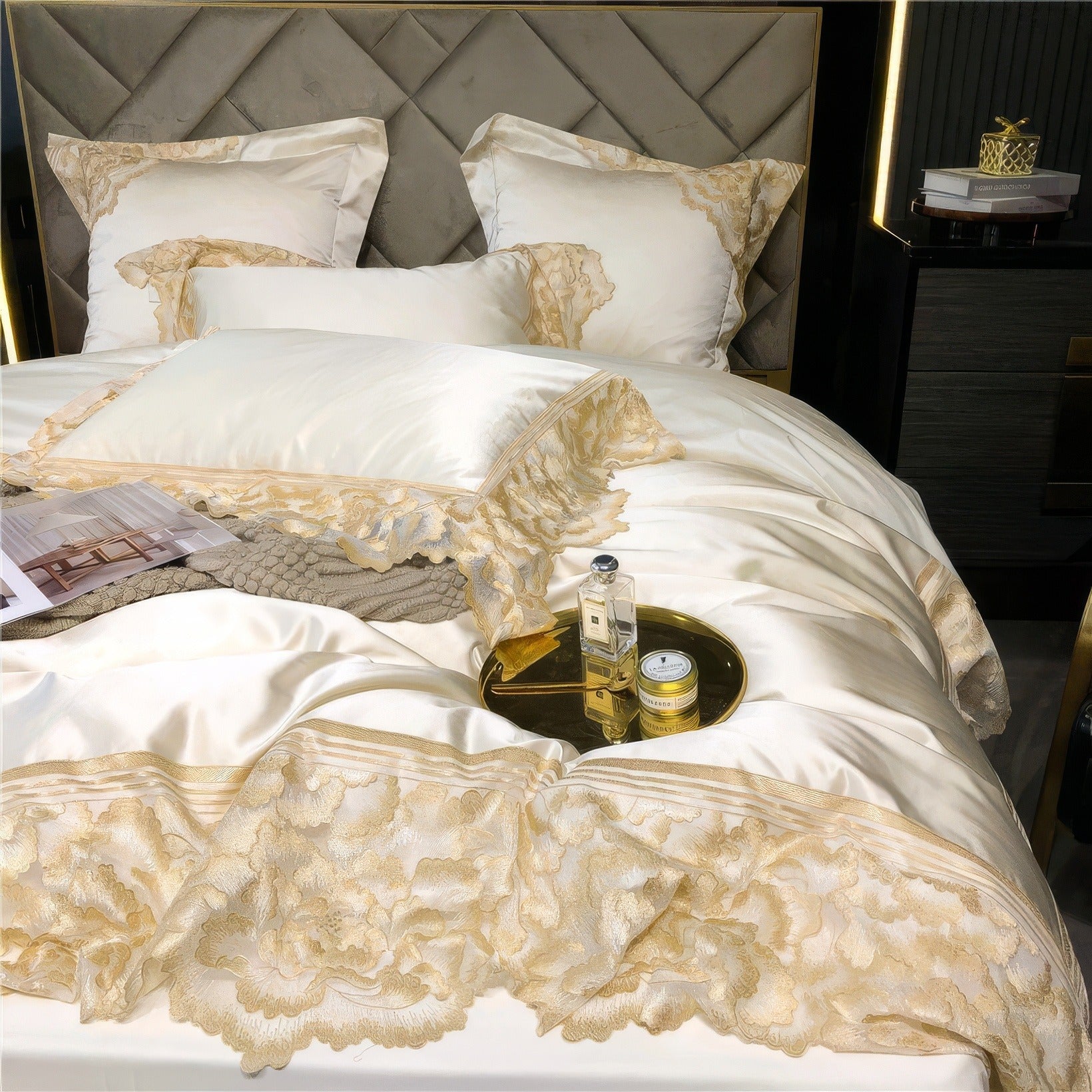 White satin bedding set with gold lace trim, featuring a decorative pillow, a gold tray holding perfume and a cream jar, and a magazine styled on a textured blanket.

