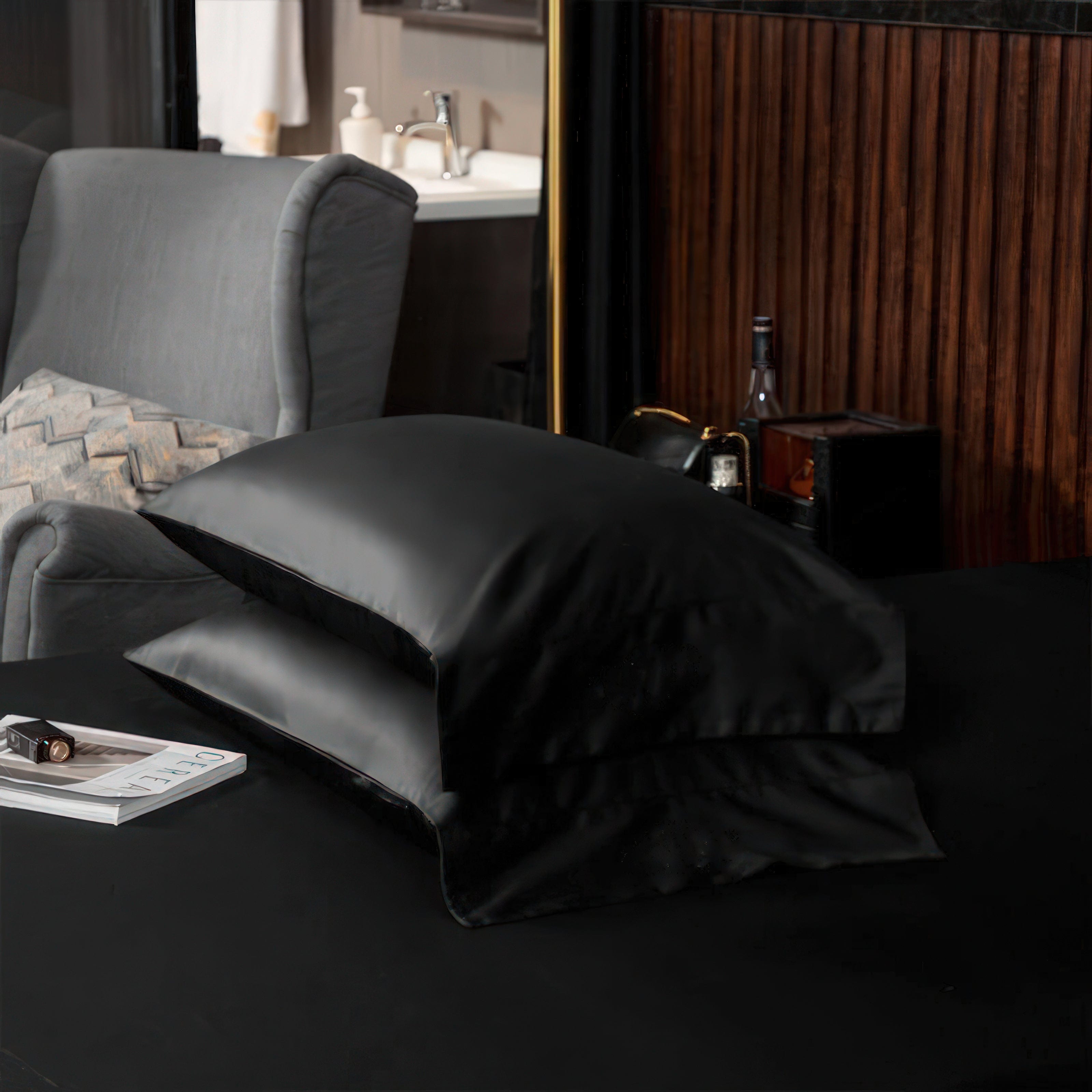 A close-up view of two neatly stacked black pillowcases on a matching black sheet, emphasizing the smooth and sleek texture of the fabric. The backdrop includes a stylish modern interior with a neutral color palette, showcasing a harmonious blend of luxury and contemporary design.

