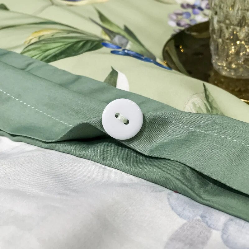 A detailed view of a green bedding set with a close-up of a white button fastener on the duvet cover, showcasing the stitching and botanical print with soft green tones in the background.

