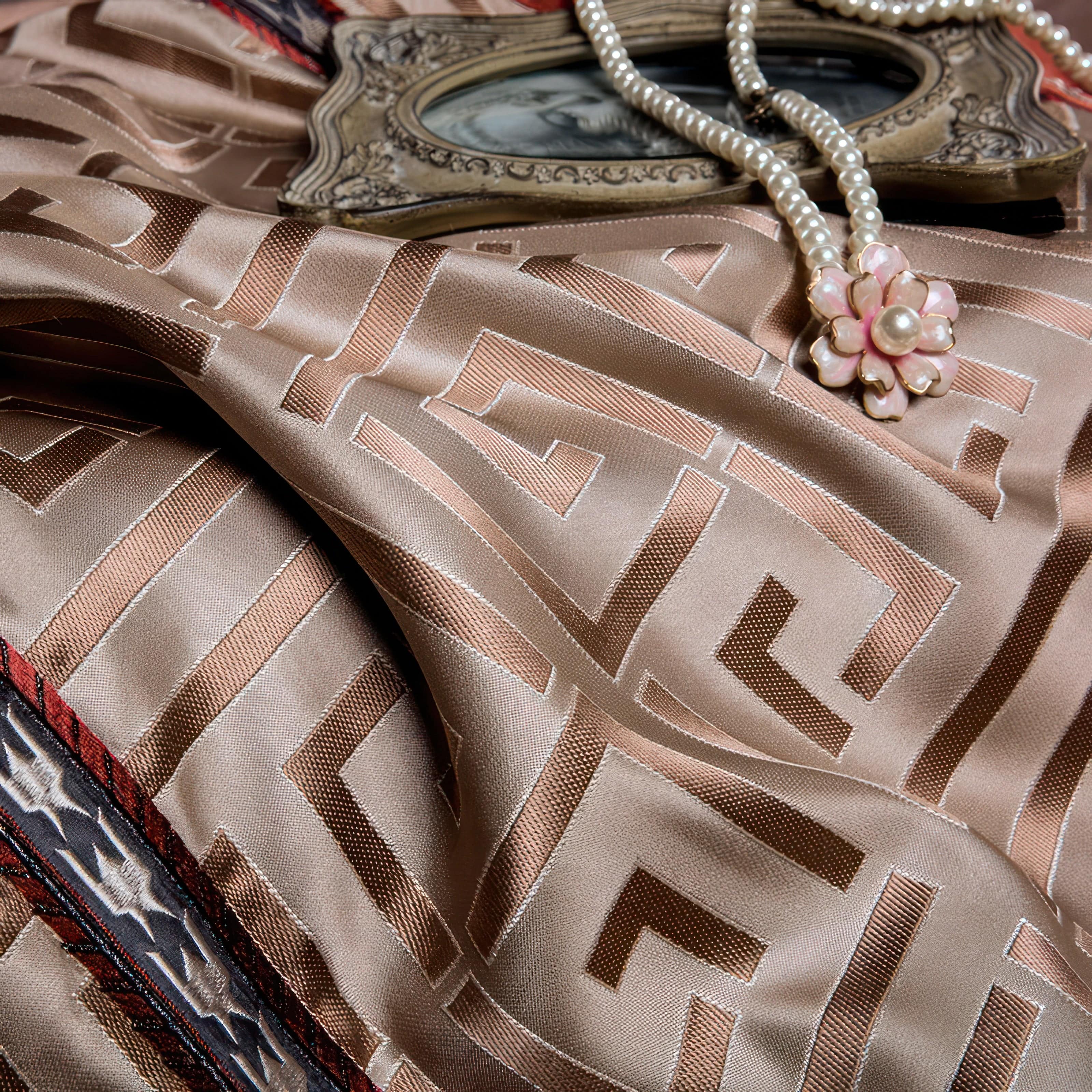 Close-up of a beige fabric with a geometric maze-like pattern, accented by red and black detailing, accompanied by a vintage-style frame and a pearl necklace with a floral pendant.