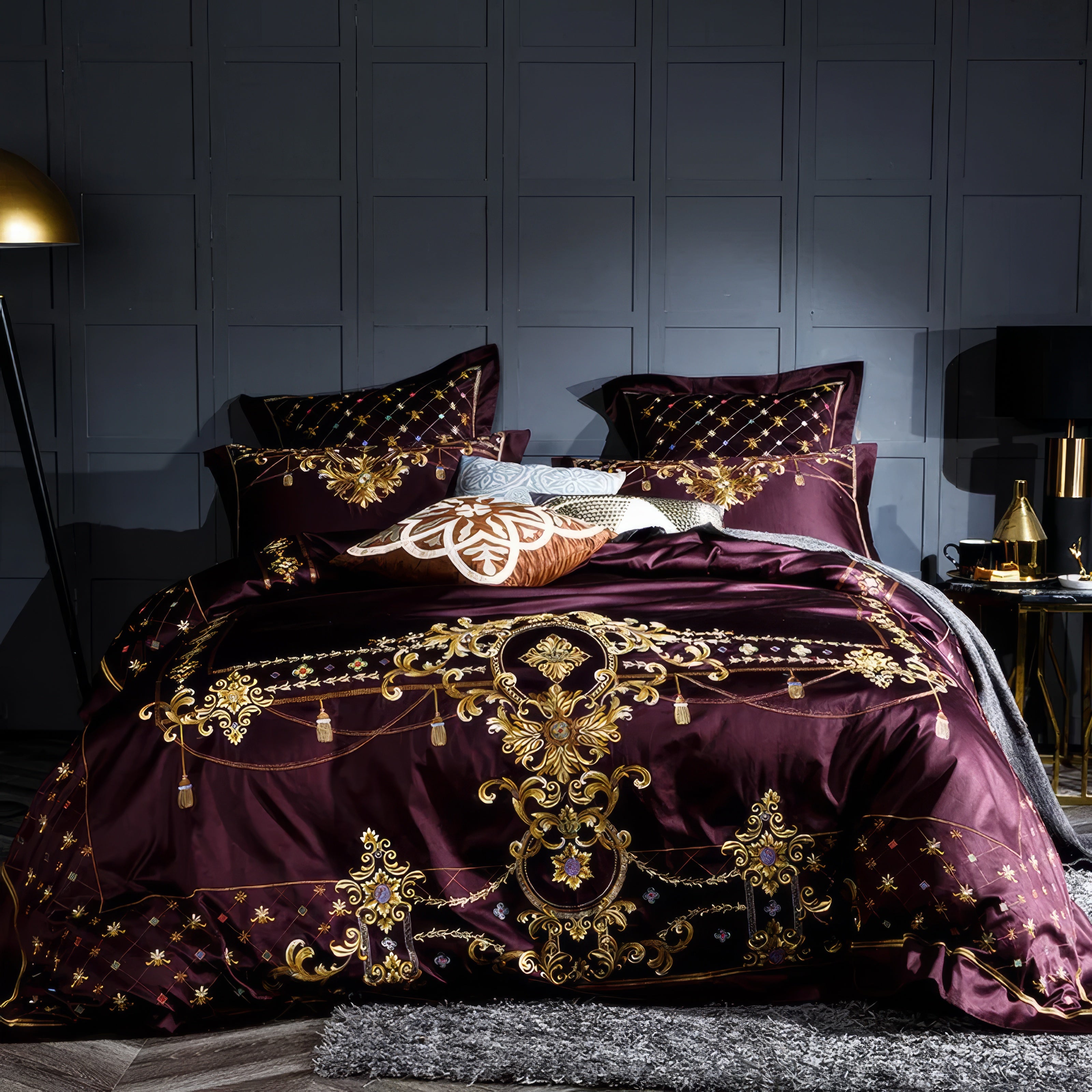 Maroon bedding set featuring elaborate gold embroidery with baroque-inspired motifs, complemented by a quilted pillow design and metallic accents. The dark background enhances the intricate golden detailing, creating an opulent and regal appearance.

