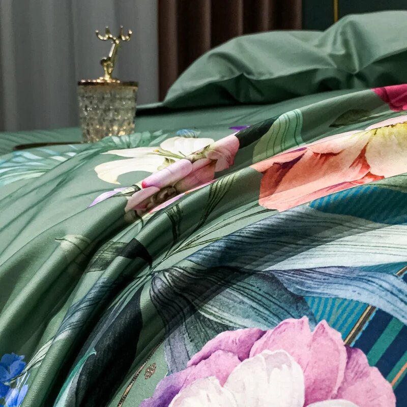 A close-up view of a luxurious Egyptian cotton bedding set, showcasing its smooth texture and vibrant floral design. The detailed flowers in bold colors such as pink, purple, and white are contrasted beautifully against the deep green background. A gold decorative tray with a crystal glass adds a touch of opulence, completing the sophisticated ambiance.

