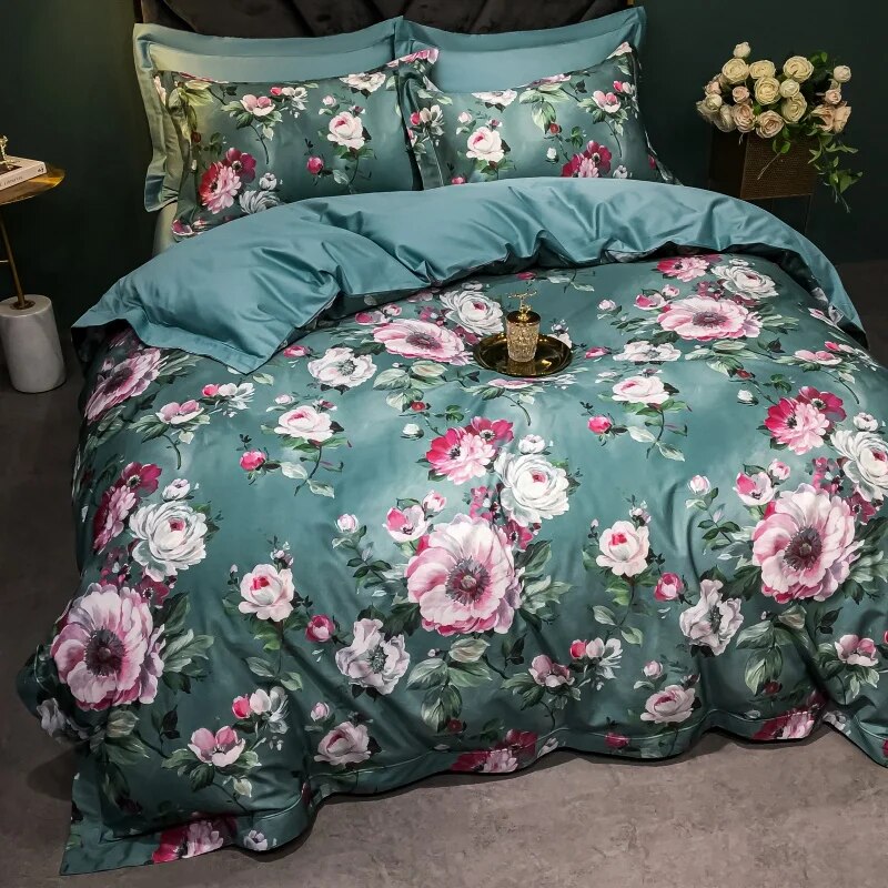 A fully styled bed featuring Egyptian cotton bedding with an elegant floral print in pink, white, and green hues on a teal base. The coordinated pillowcases and duvet cover are complemented by a soft sheen and luxurious draping, creating a sophisticated and cozy ambiance.

