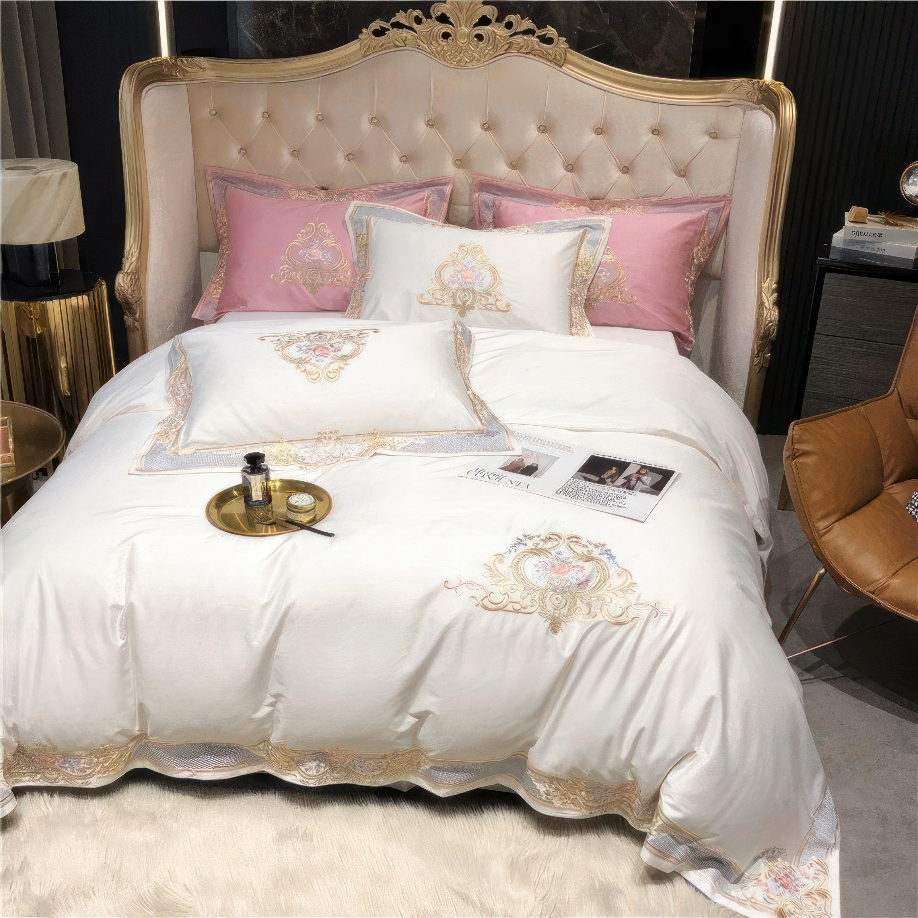 An elegant bedding set featuring a luxurious white duvet cover and pillows with intricate gold embroidery and pastel pink accent pillows. The design exudes sophistication, complemented by a tufted cream headboard with a golden frame, creating a regal ambiance. The setup includes a plush white rug, a gold-toned tray with accessories, and a leather accent chair, balancing opulence and modernity.

