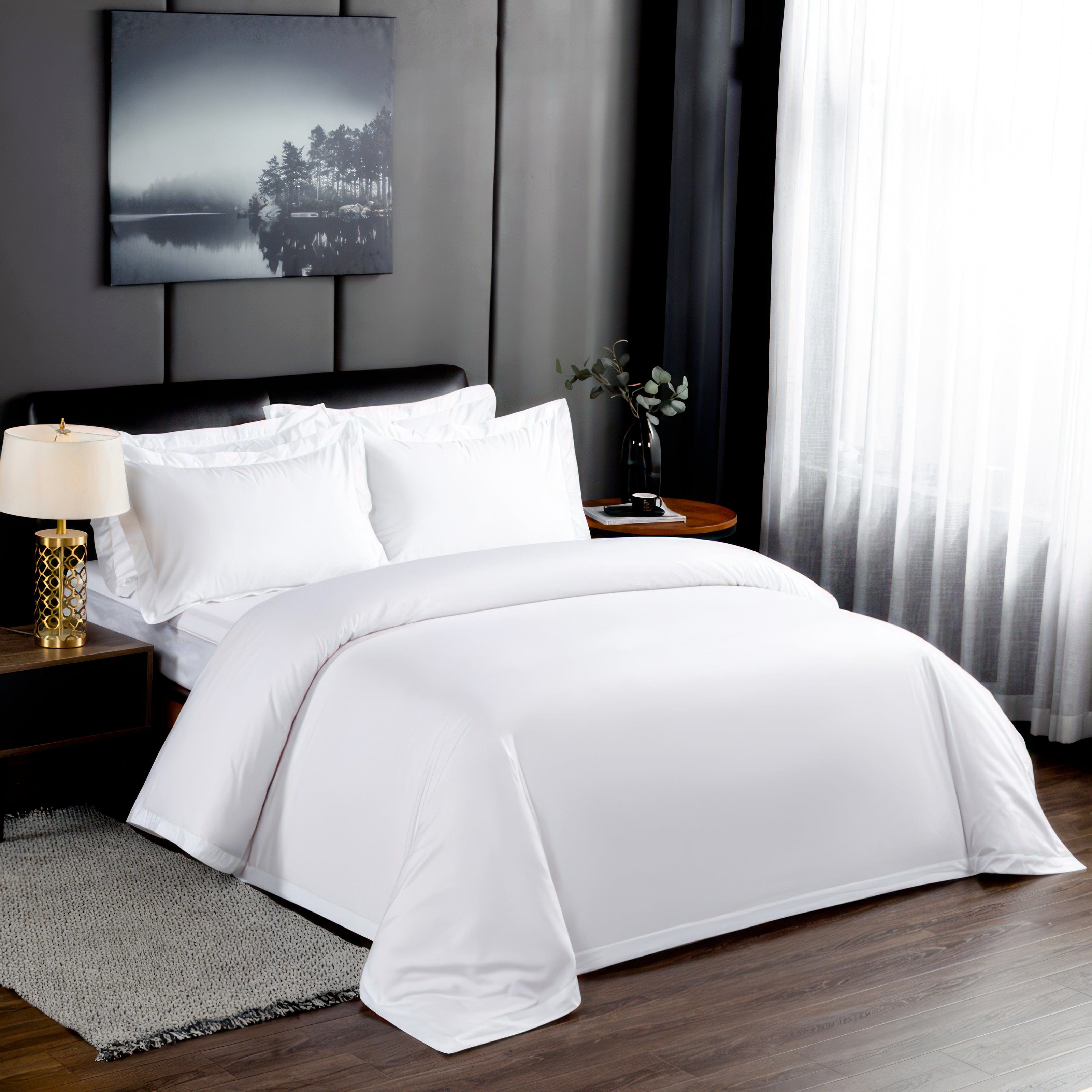 Elegant white bedding set with a clean, crisp finish, arranged neatly on a dark wooden bed frame. The backdrop features modern, minimalist decor with a serene landscape painting, gold-accented lamp, and soft white curtains filtering natural light.

