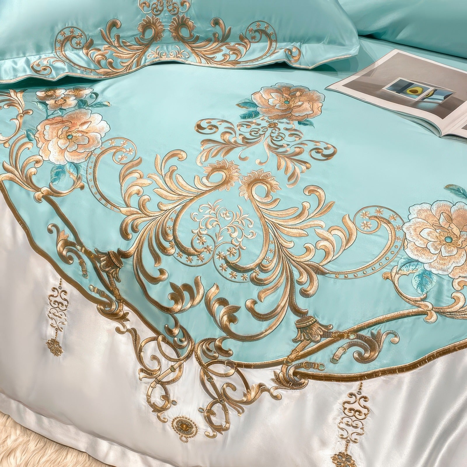 Close-up of an aqua duvet cover adorned with intricate gold embroidery and floral motifs in pastel hues of pink and green. The elegant design is complemented by a luxurious white border, adding a regal touch. A book rests casually on the bed, enhancing the inviting ambiance.

