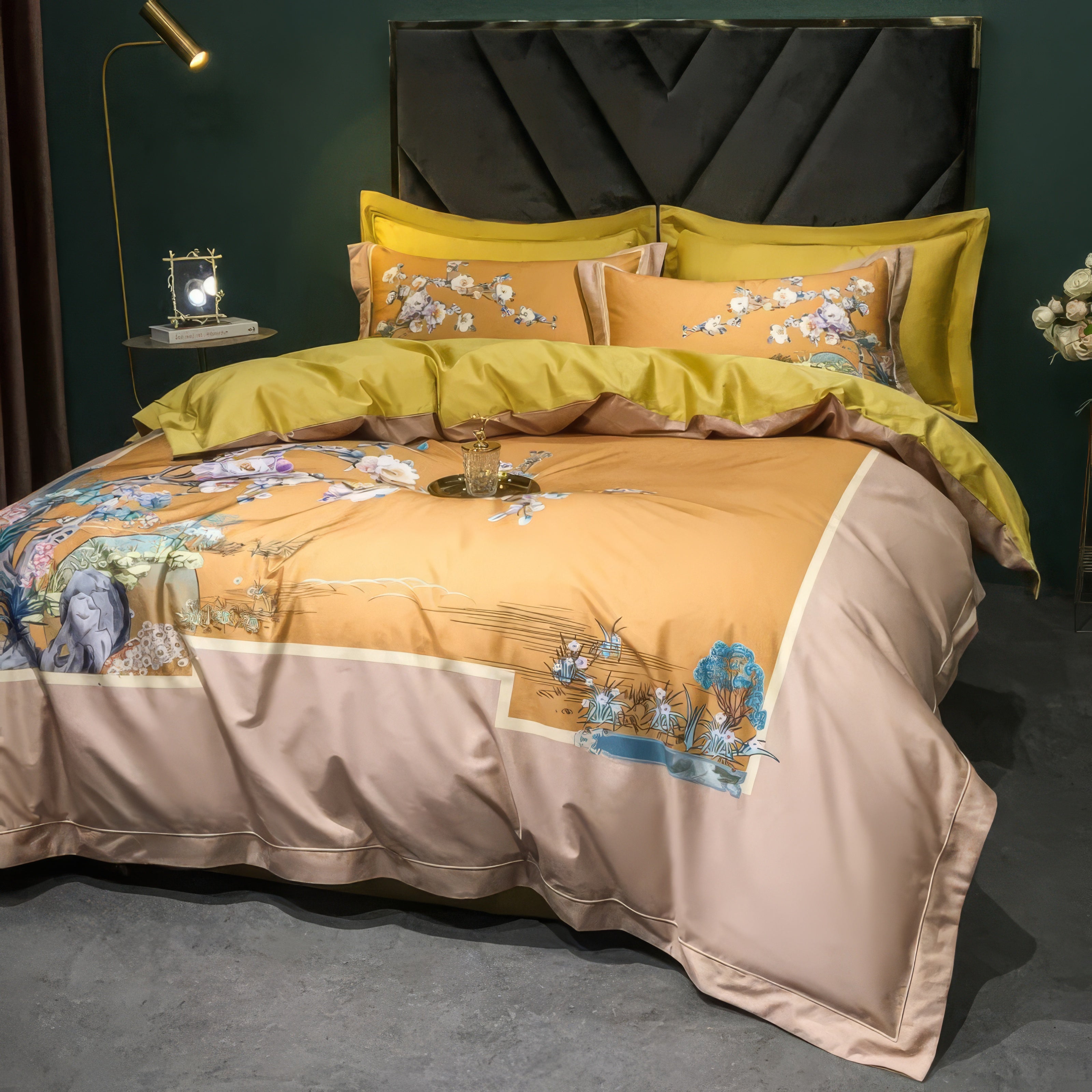 Amber satin bedding set with floral embroidery featuring white cherry blossoms, teal leaves, and nature-inspired accents. The bed is styled with yellow pillowcases, a matching top sheet, and a decorative headboard. A gold floor lamp and a small nightstand with a clock add elegance to the bedroom, while the green wall provides a modern contrast.

