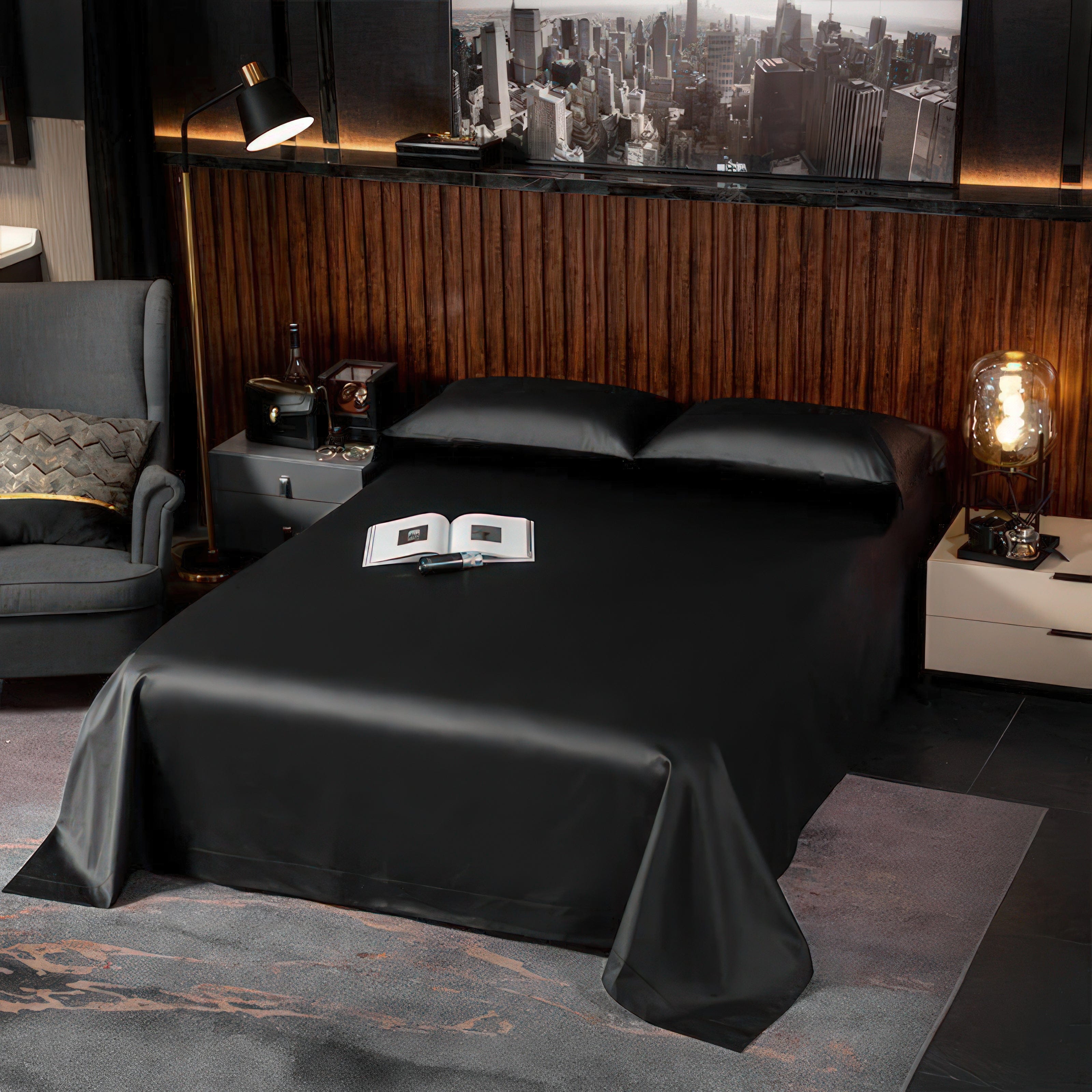 A sleek black bedspread draped over a bed with matching black pillowcases, exuding a minimalist yet luxurious aesthetic. The surrounding modern room features a wood-paneled backdrop, cityscape artwork, and contemporary furniture, highlighting a sophisticated ambiance.

