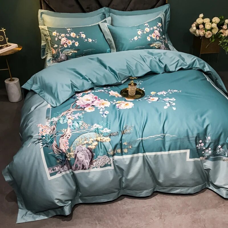 Teal bedding set featuring an intricate floral and landscape design with cherry blossoms, branches, and a nature-inspired scene including rocks and trees. The duvet cover is bordered with a white accent line, complementing the elegant floral motifs. Matching pillowcases carry the same design theme. A gold tray with an ornate ornament is placed on the bed, and a vase with white roses is visible in the background, enhancing the luxurious setting.

