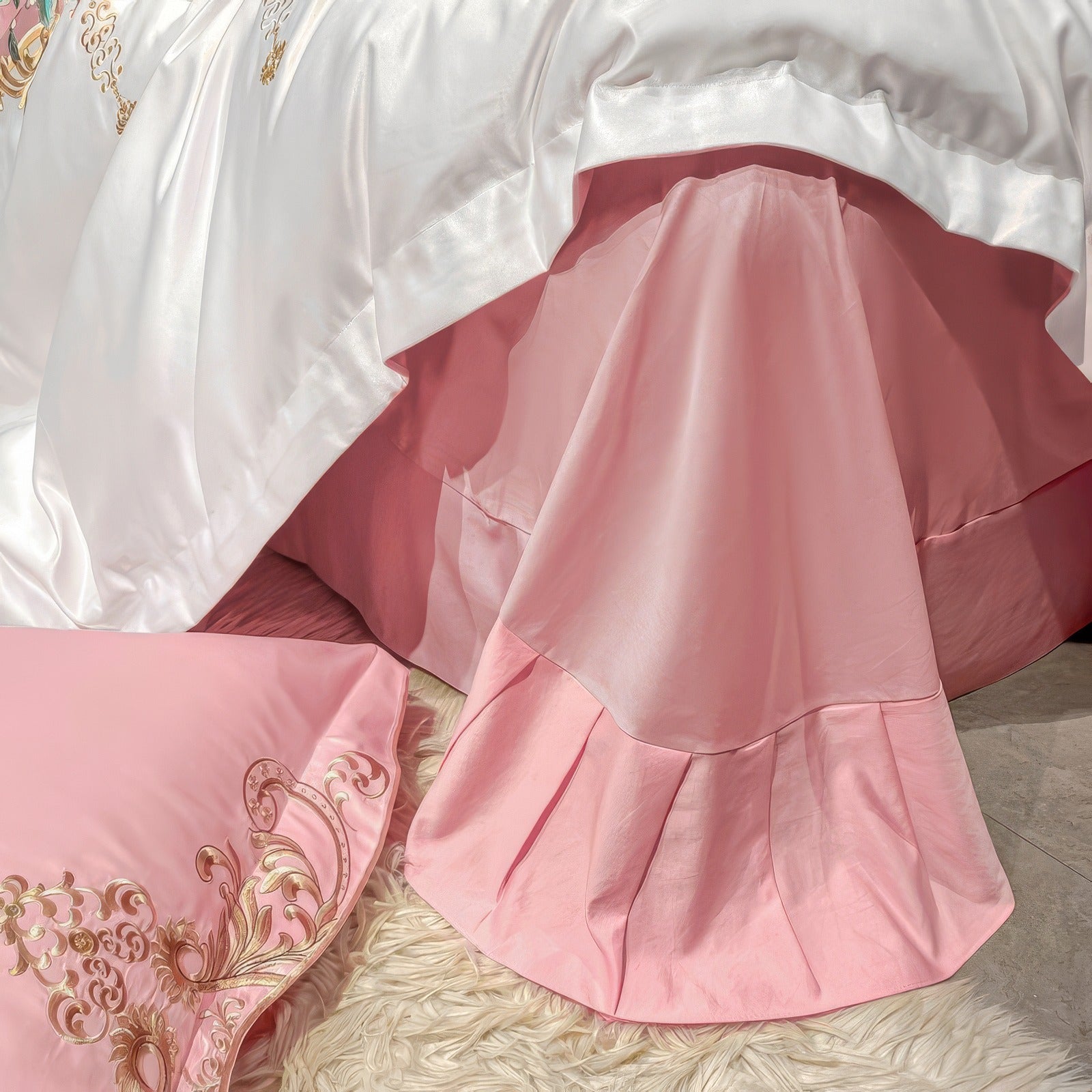 A detailed view of a luxurious bed ensemble featuring a white satin duvet cover draped elegantly over a soft pink bed skirt with pleated details. A matching pink pillowcase with intricate gold embroidery lies on a plush cream-colored rug, adding texture and warmth to the scene. The layered fabrics highlight a harmonious combination of colors and textures, creating an opulent and inviting bedroom aesthetic.

