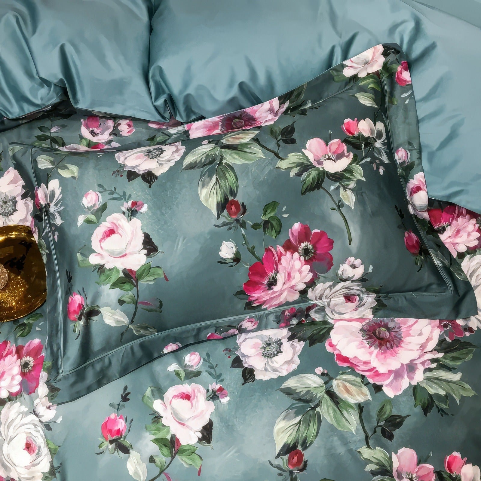 Close-up of a pillowcase made from luxurious Egyptian cotton, adorned with vibrant floral prints in shades of pink, white, and green against a teal background. The fine stitching and soft sheen enhance the premium quality, paired beautifully with coordinating bedding.

