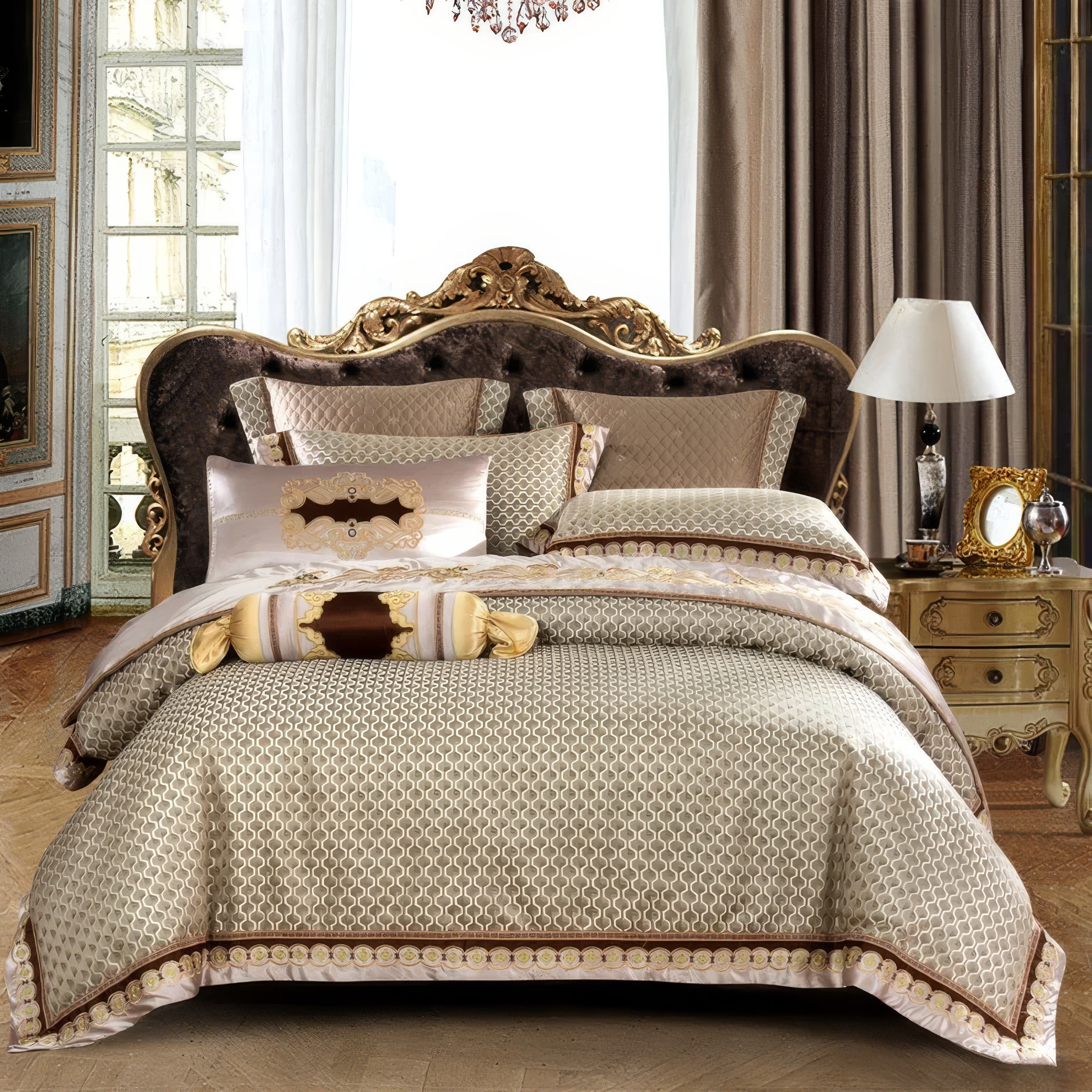 A luxurious beige and brown bedding set featuring intricate geometric patterns and ornate gold accents. The bed is styled with matching decorative pillows, including bolsters, and a plush headboard with carved gold detailing. The backdrop includes elegant floor-length curtains and a vintage-style nightstand with a table lamp and ornate decor, exuding a classic and sophisticated ambiance.

