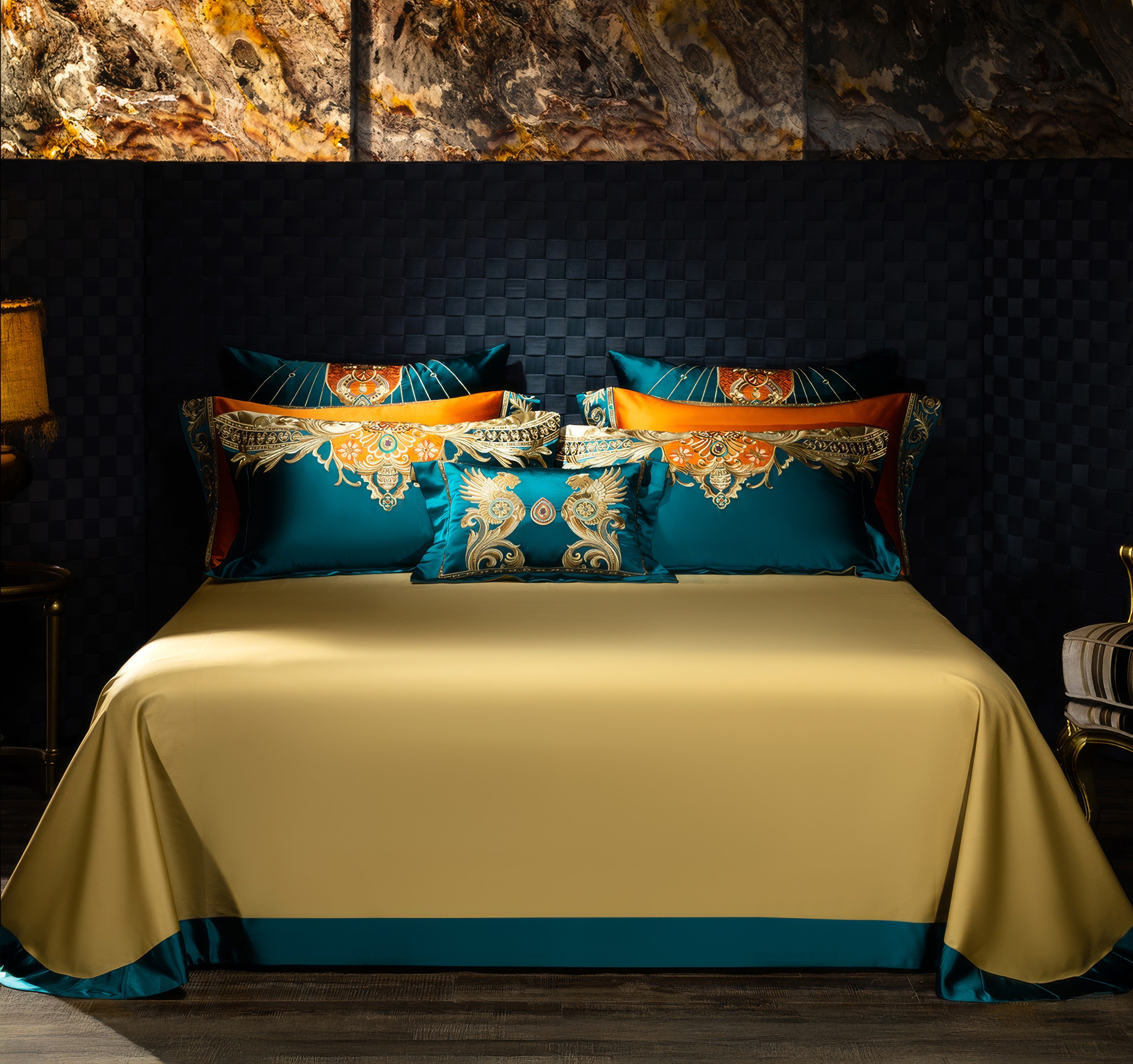 Elegant bedding set featuring a golden satin bedspread with teal and orange accents, paired with pillowcases and a decorative throw pillow showcasing intricate gold and turquoise embroidery, styled in a luxurious bedroom with a dark textured wall and marble details.