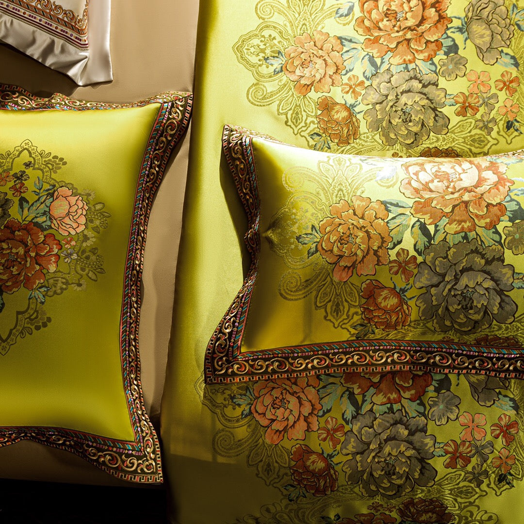 A close-up view of a lime green bedding set showcasing its intricate floral patterns in vibrant shades of orange, green, and yellow, accentuated by delicate lace motifs. The pillows and duvet feature ornate gold and red embroidered borders, adding a luxurious touch to the design. The rich detailing and vibrant color scheme exude elegance and sophistication.