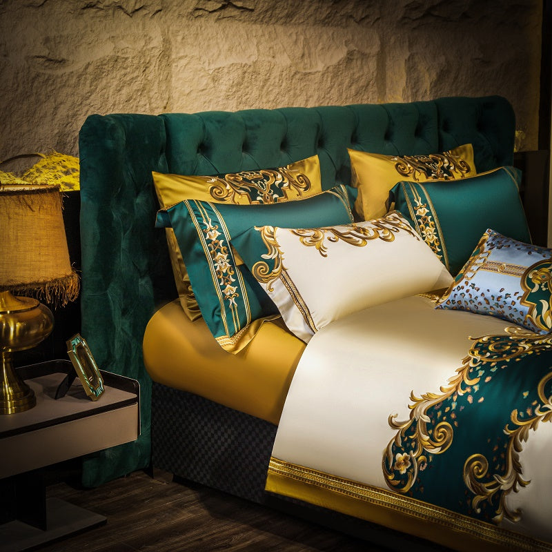 Luxurious bedding set featuring rich green and gold tones with ornate baroque embroidery, paired with matching pillowcases. Showcased in an opulent bedroom with a velvet tufted green headboard, a gold-accented bedside lamp, and a rustic stone-textured wall, creating a regal and elegant atmosphere.