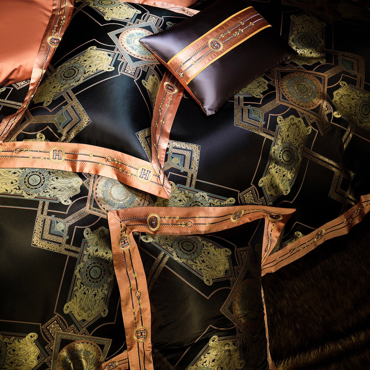 A top-down view of an intricately designed luxury bedding set. The fabric features a striking black base with a geometric pattern interlaced with gold and copper accents, creating an opulent and regal look. The bedding is adorned with a satin copper-toned border that includes chain-like embroidery and "H" monograms for a sophisticated touch. A decorative pillow in a deep chocolate brown shade complements the set, featuring a matching copper and gold ribbon detail. The ensemble exudes elegance and grandeur, 