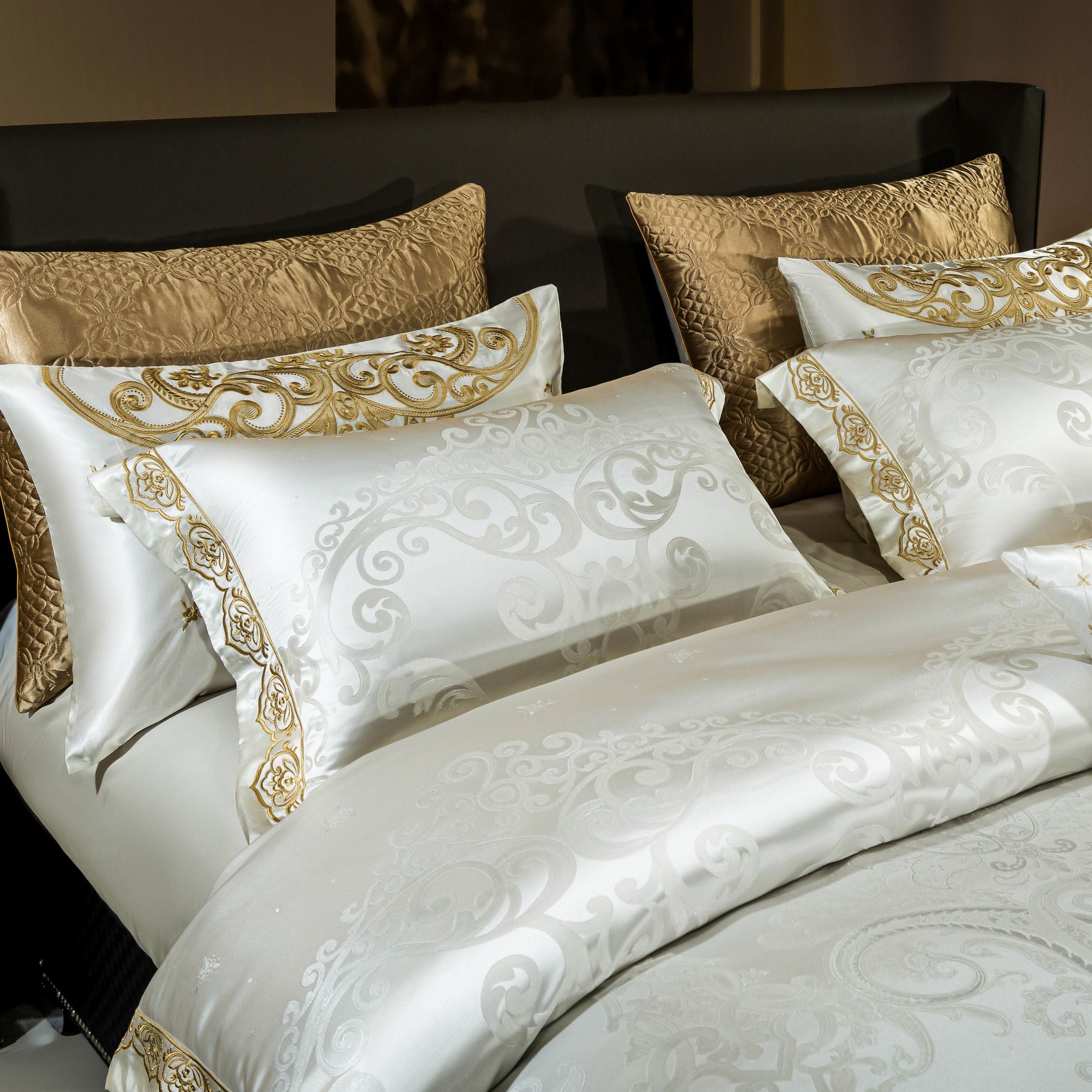 A detailed close-up of luxurious white bedding adorned with gold embroidered patterns on pillowcases and duvet edges. The golden jacquard pillows add texture and richness, creating a regal and sophisticated aesthetic. The intricate swirls and motifs in the embroidery enhance the opulent charm, ideal for a high-end bedroom setting.

