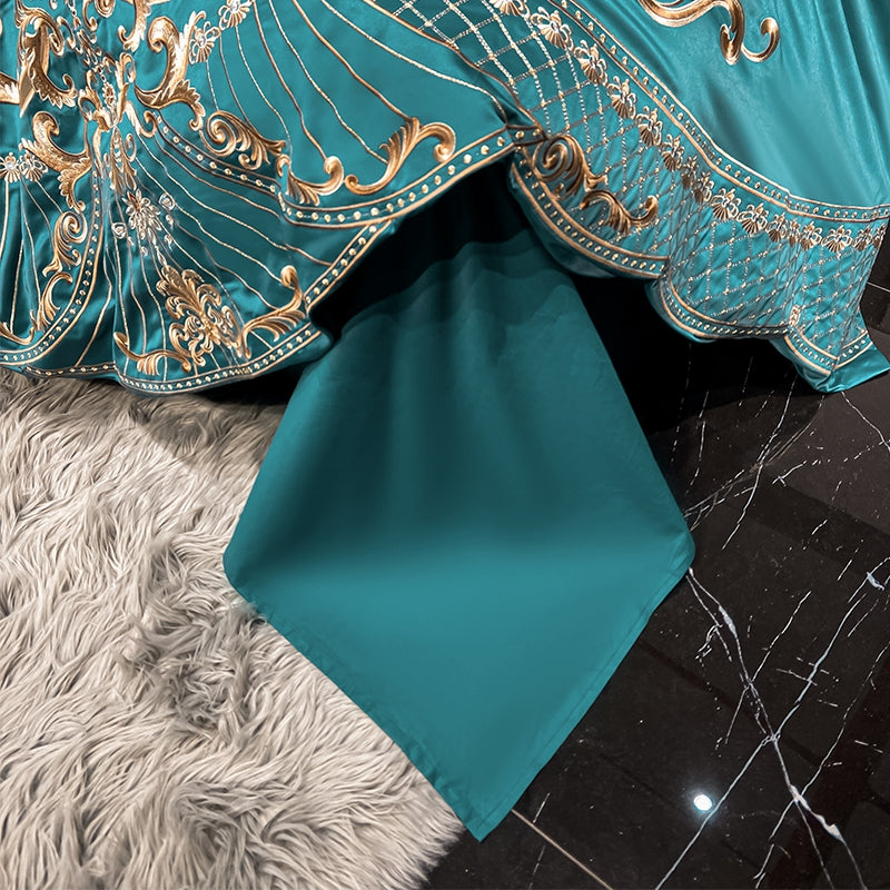 The corner of a teal bedding set drapes elegantly over a plush grey rug and glossy black marble flooring. The fabric features intricate gold embroidery with ornate patterns near the edge, while the solid teal section flows smoothly to the floor, showcasing a luxurious and polished finish.

