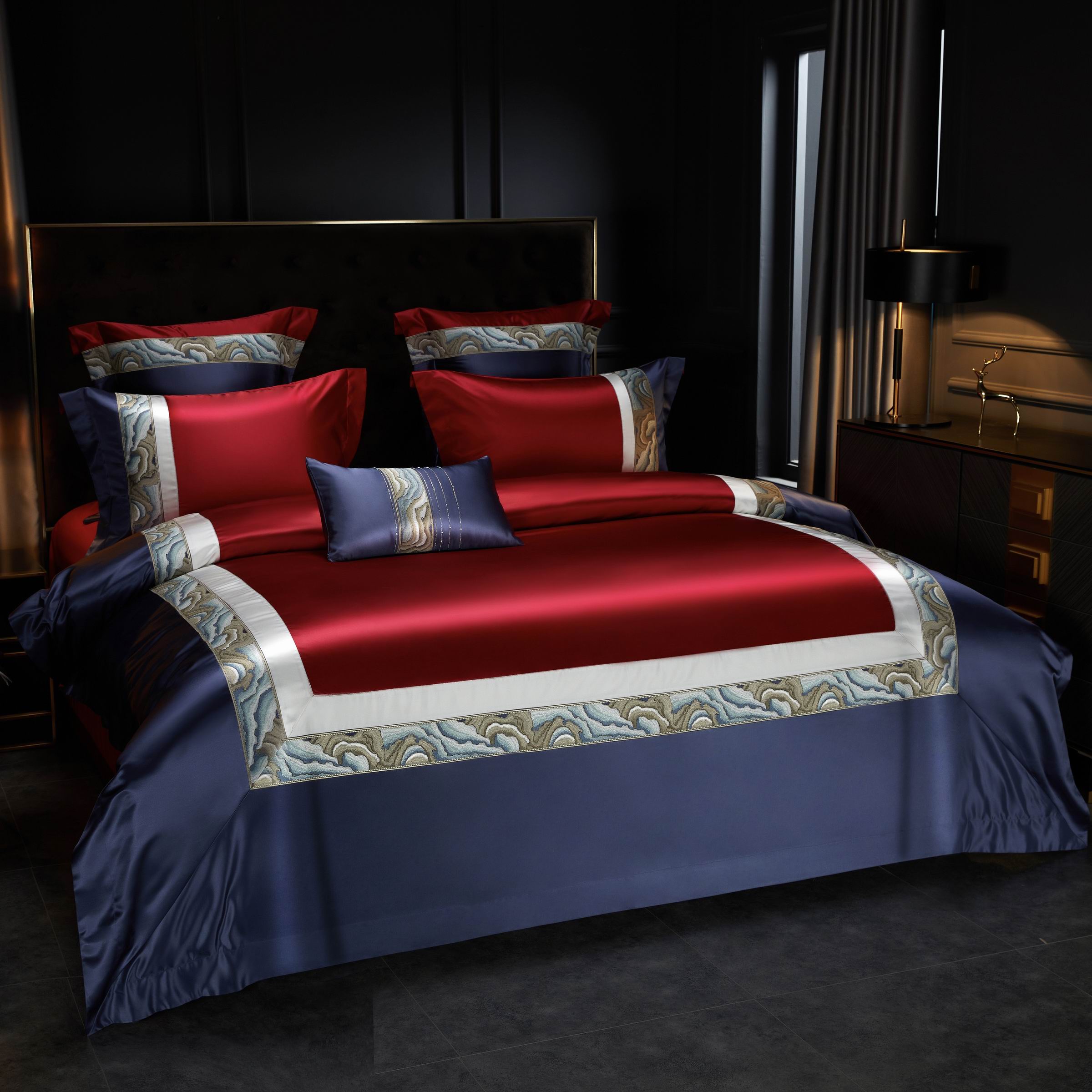 The bedding set combines bold burgundy and navy hues, highlighted by intricate marble-inspired borders in soft blues and greys. The red duvet cover serves as the centerpiece, framed by clean white and detailed trim that adds elegance. Matching pillowcases and a decorative navy bolster pillow with subtle marble accents enhance the coordinated look. Set against a dark, modern bedroom backdrop, the design exudes opulence and sophistication.