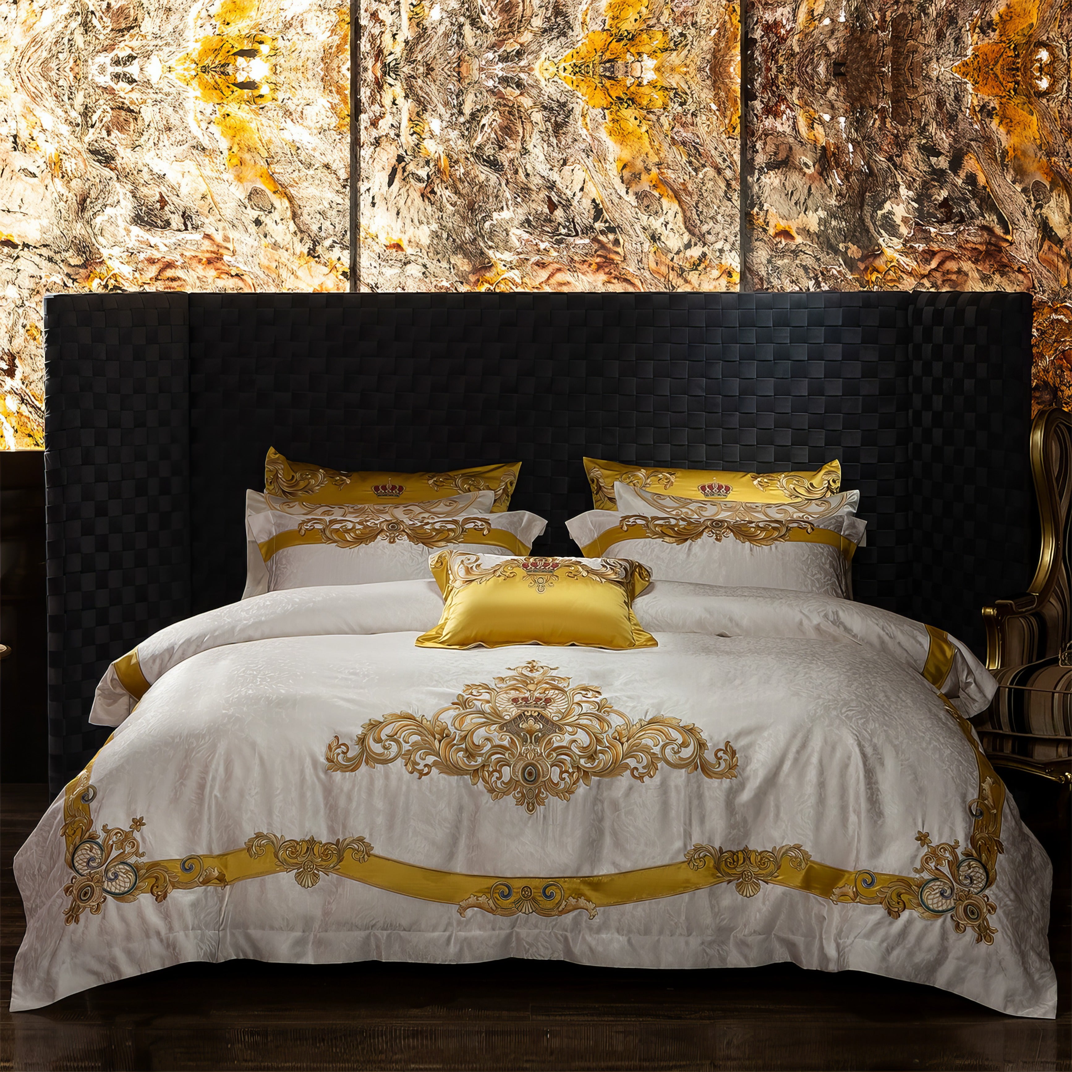 A luxurious bedding set showcasing intricate golden embroidery on a pristine white base. The design features regal crown motifs and ornate baroque patterns, accentuated with vibrant gold trims. Included are matching pillowcases and a golden decorative pillow, enhancing the grandeur. The textured duvet adds depth, while a warm lamp on a brass side table completes the elegant ambiance. Perfect for a majestic and opulent bedroom setting.