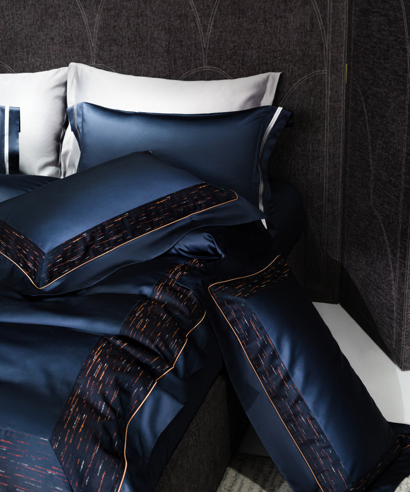 Refined navy blue bedding featuring detailed streak accents in copper tones. The sleek duvet and matching pillowcases showcase a rich sheen, complemented by fine stitching and contrasting piping for a modern, luxurious aesthetic.

